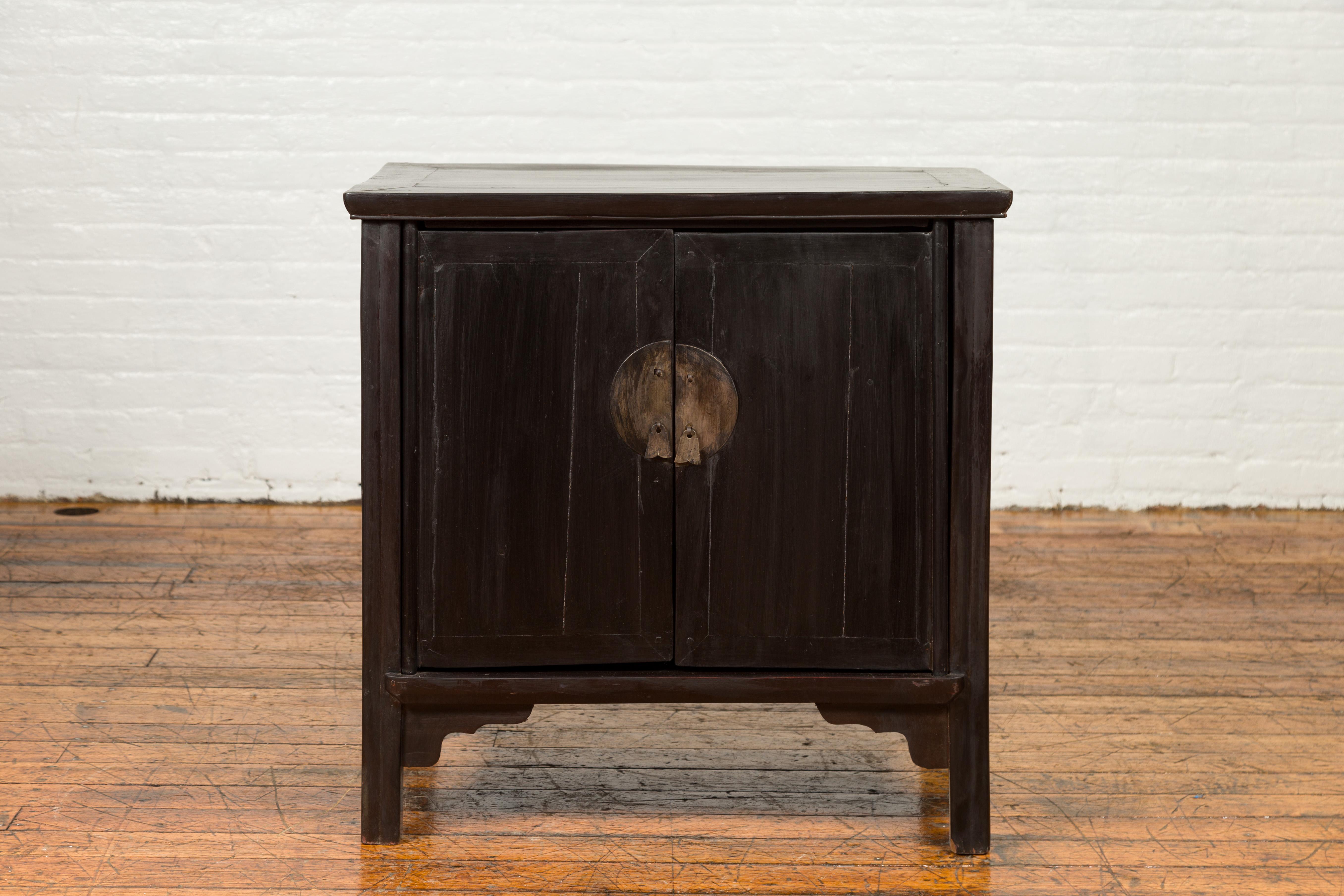 A Chinese vintage Ming Dynasty style side cabinet from the mid-20th century, with round medallion hardware and dark brown patina. Created in China during the midcentury period, this side cabinet features a rectangular top with central board and