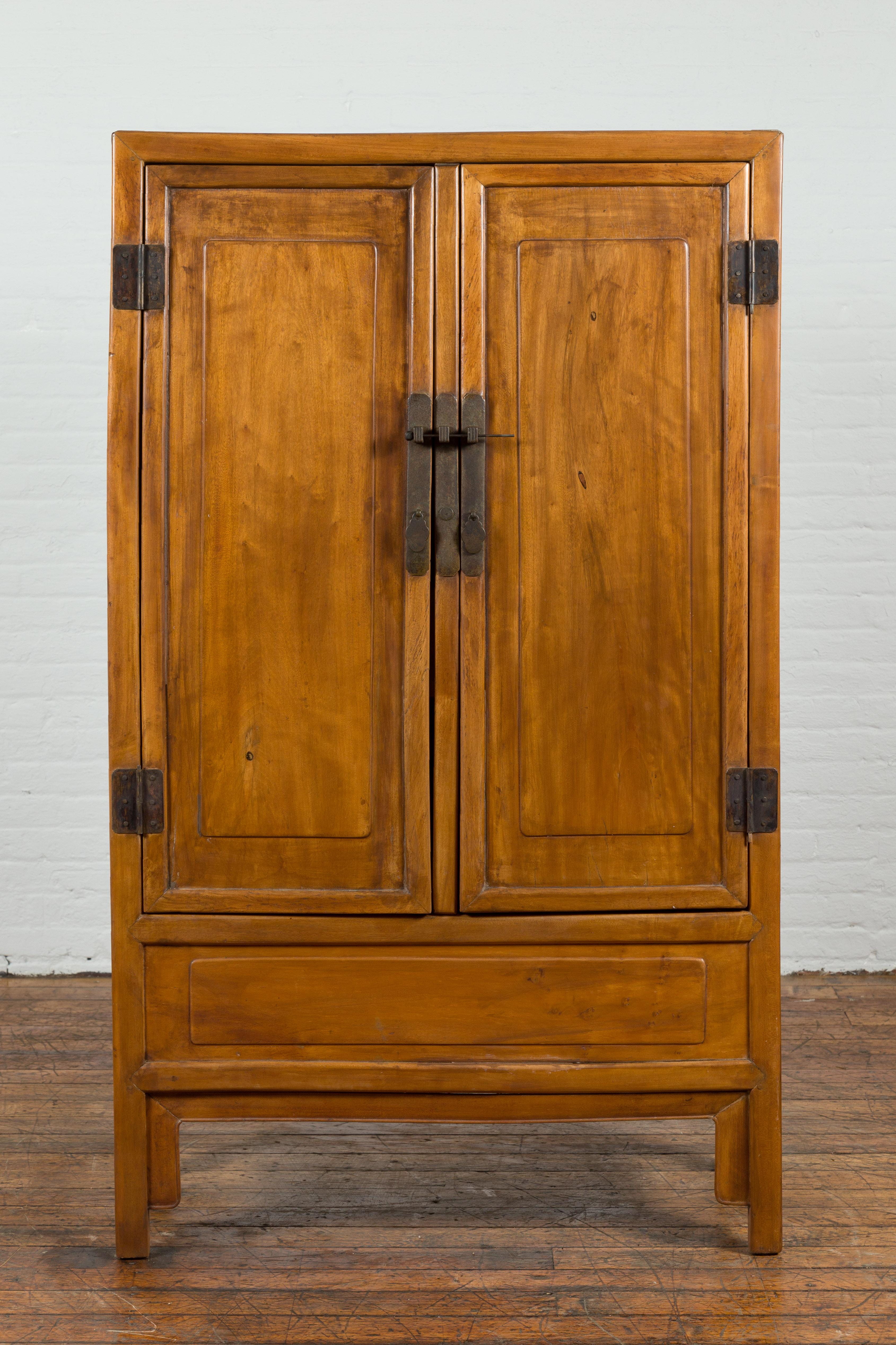 A Chinese vintage natural elmwood cabinet from the mid 20th century, with brass hardware and hidden drawers. Created in China during the midcentury period, this cabinet features a linear silhouette perfectly complimented by a natural elm patina. The