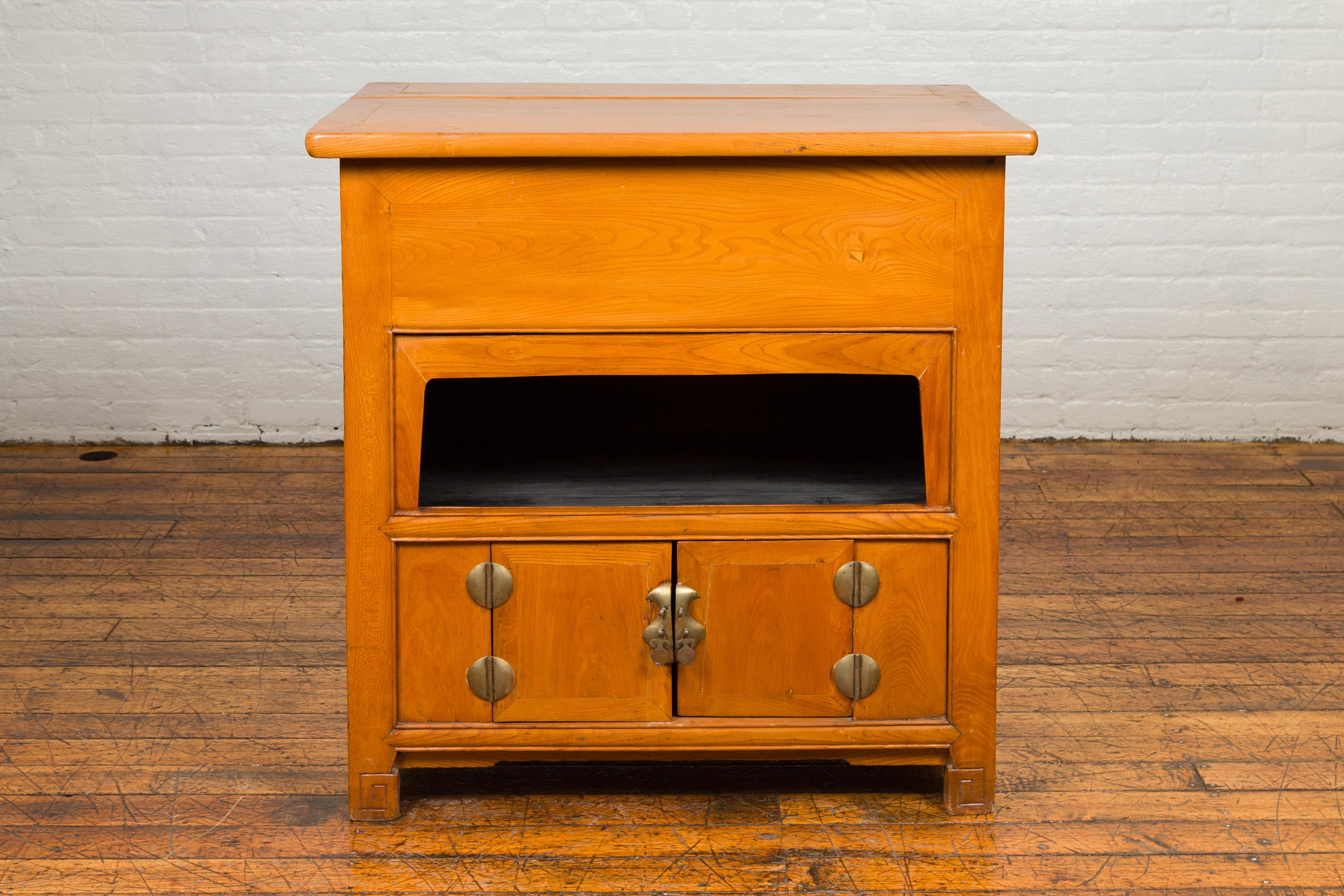 A Chinese vintage natural elmwood console cabinet from the mid-20th century, with removable top, open shelf, double doors and bronze hardware. Crafted in China during the midcentury period, this elm cabinet features a two-part rectangular top whose