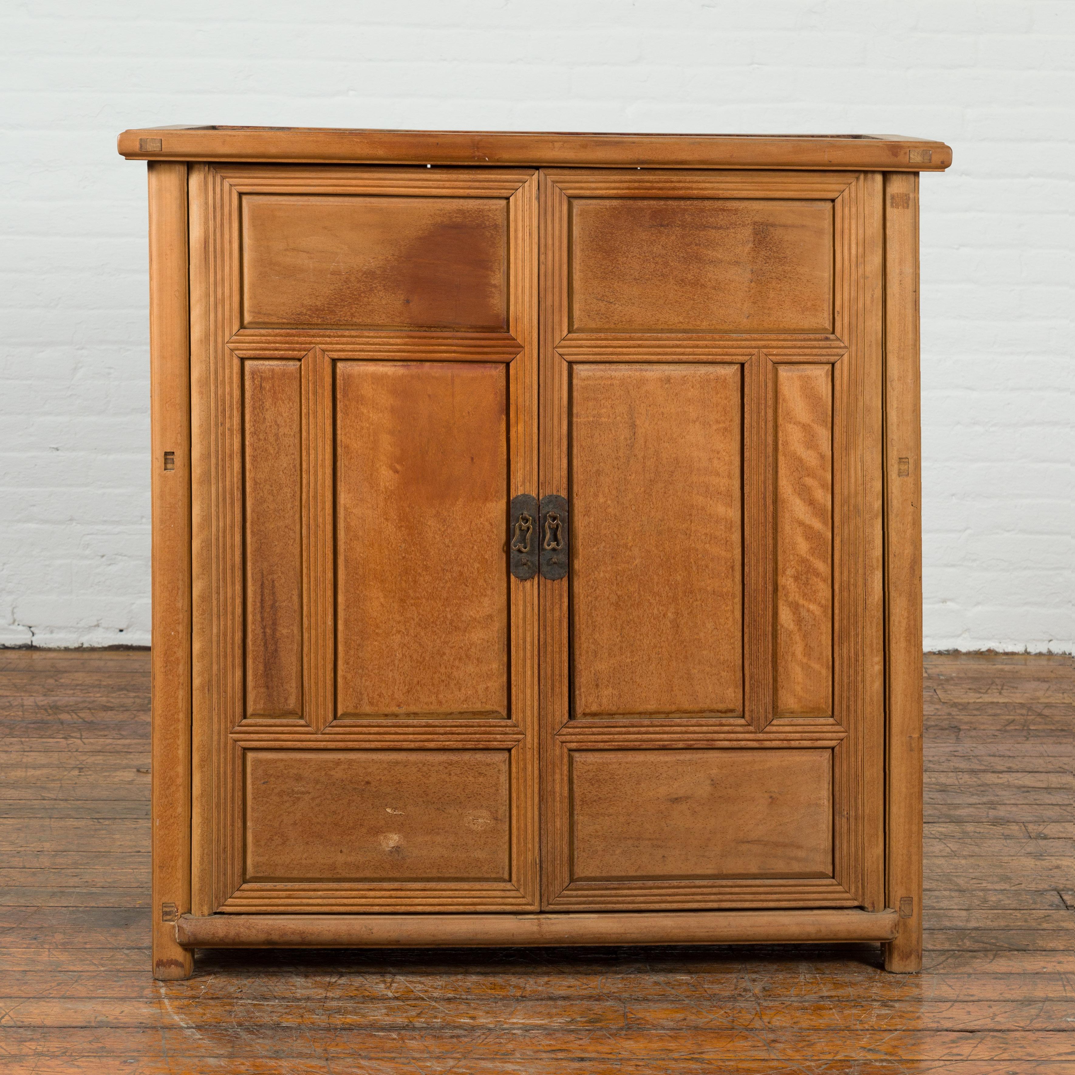 A Chinese vintage natural wood finish cabinet from the mid 20th century with two doors and hidden drawers. Created in China during the midcentury period, this cabinet features a linear silhouette perfectly complimented by a natural wood finish. The