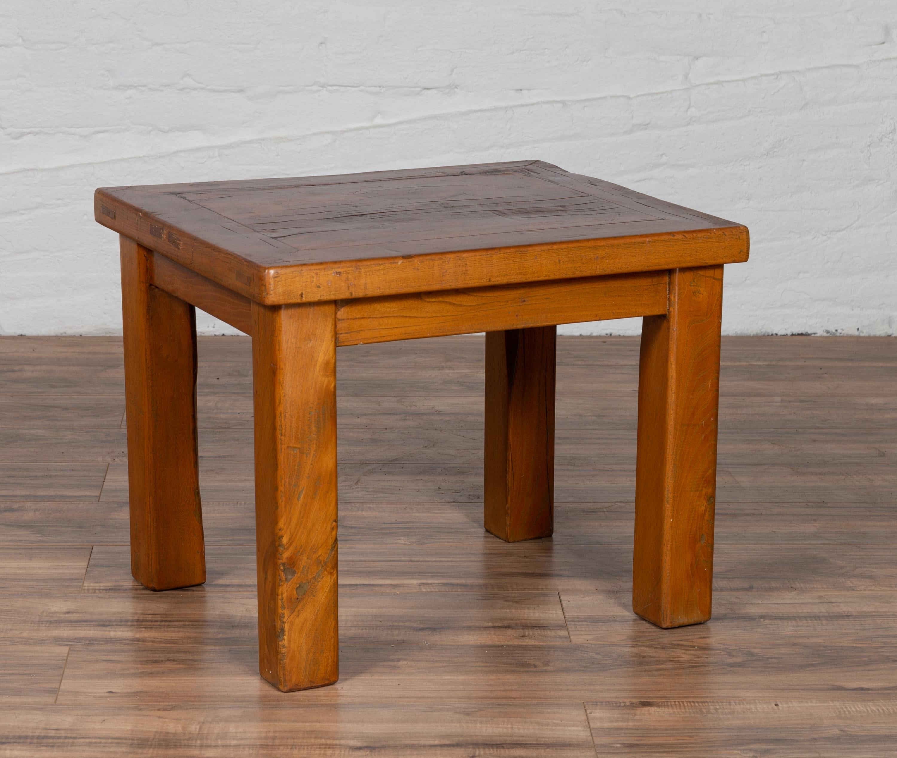A Chinese vintage natural wood side table from the mid-20th century with square legs and contemporary design. Born in China during the midcentury period, this elegant side table features a rectangular top with central board, sitting above a linear