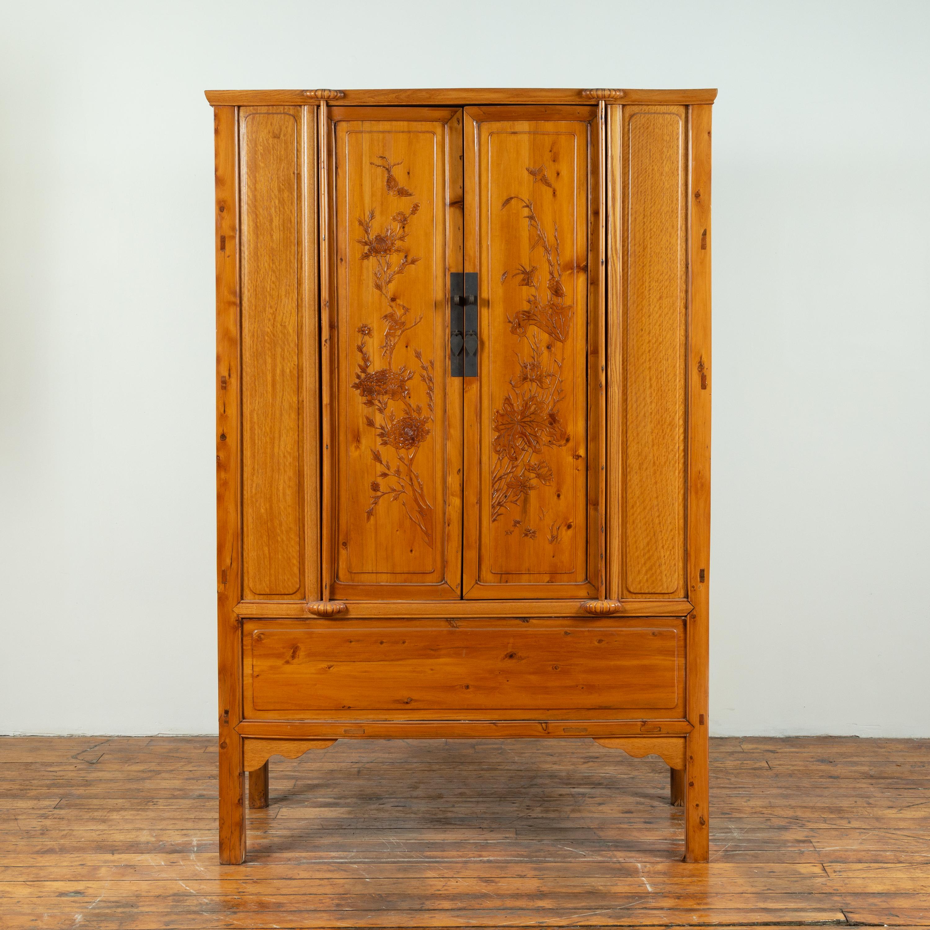 A Chinese vintage Ming Dynasty style natural wood two-door cabinet from the mid-20th century, with floral décor and hidden drawers. Born in China during the midcentury period, this exquisite wooden cabinet features a clean silhouette, perfectly