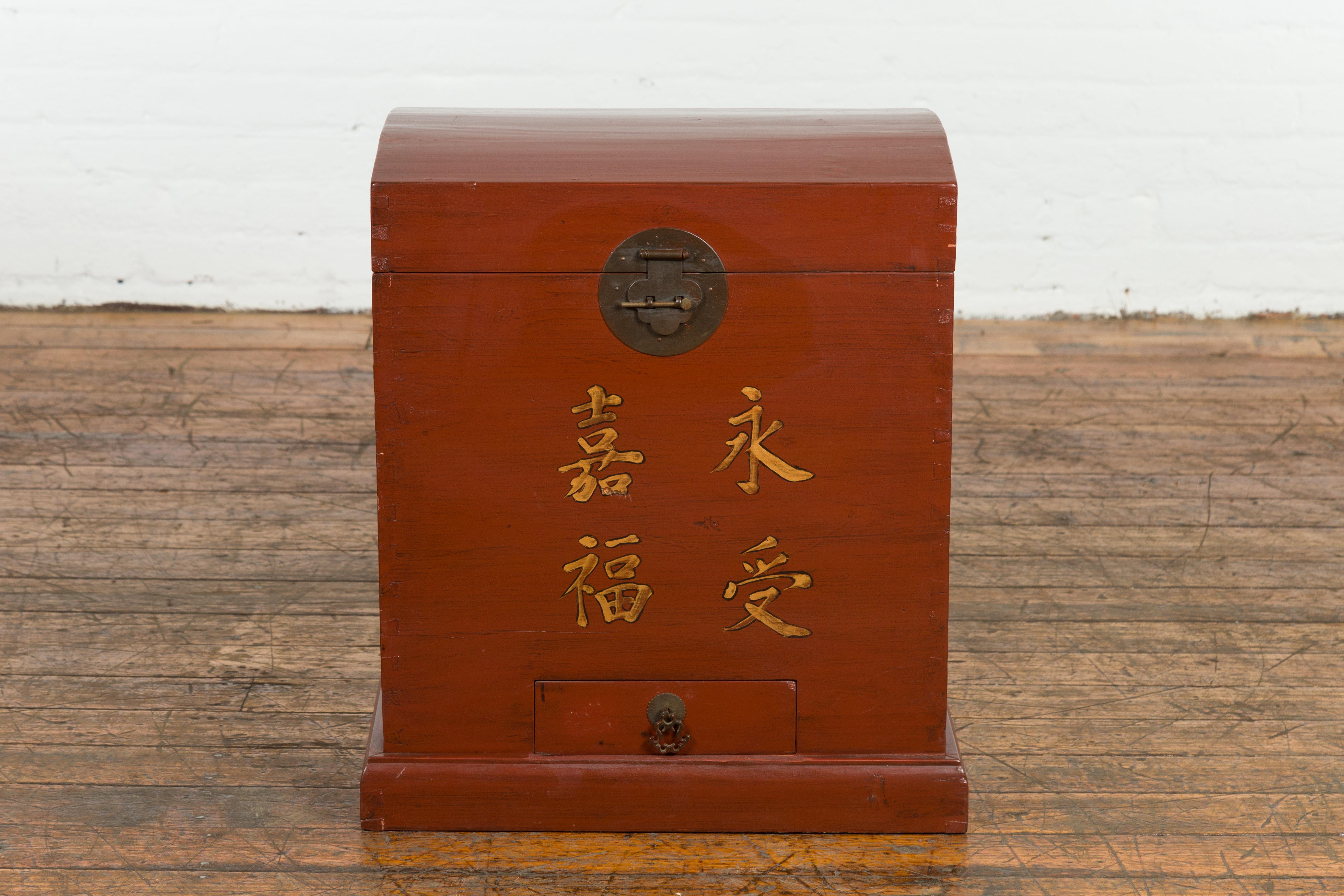 A vintage Chinese red lacquer wedding chest from the Mid-20th Century with gilded calligraphy, low drawer and brass hardware. Created in China during the midcentury period, this wedding chest showcases a red lacquer perfectly complimenting its clean