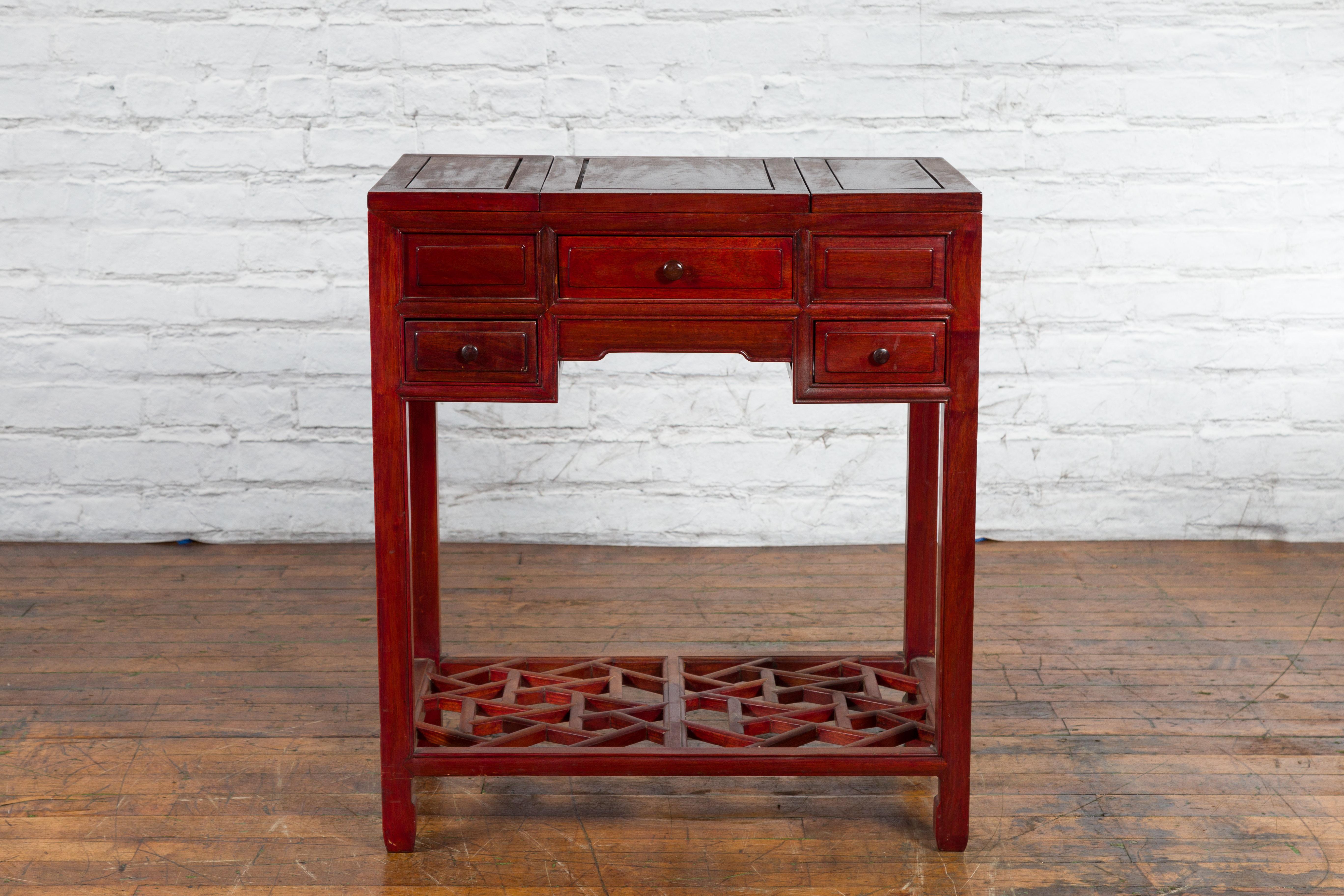 A vintage Chinese red lacquer three-drawer vanity table from the mid-20th century with folding mirror top and dual opening sides. Created in China during the mid-century period, this vanity table features a three-piece hinged rectangular top, made