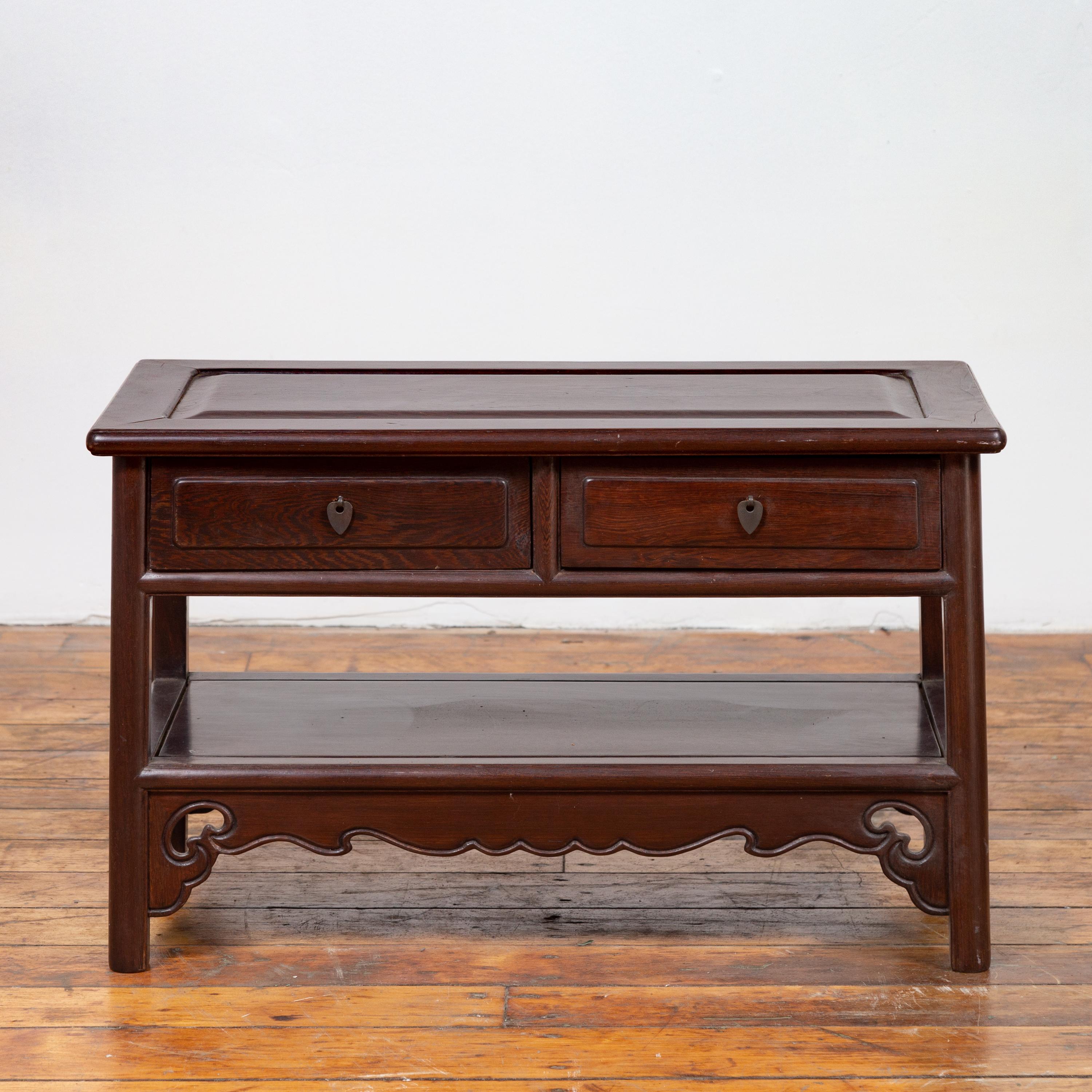 A Chinese vintage rosewood low side table from the mid-20th century, with two drawers, shelf and scalloped skirt. Born in China during the midcentury period, this elegant rosewood table features a rectangular top with raised central board, sitting