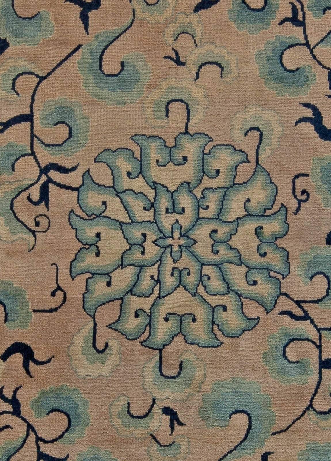 This vintage Chinese rug features an all-over design of floral motifs and cloud bands in shades of light and inky blue against a field of beige, circa 1920. A repeating swastika pattern, a staple of vintage Chinese carpets, composes the main border.