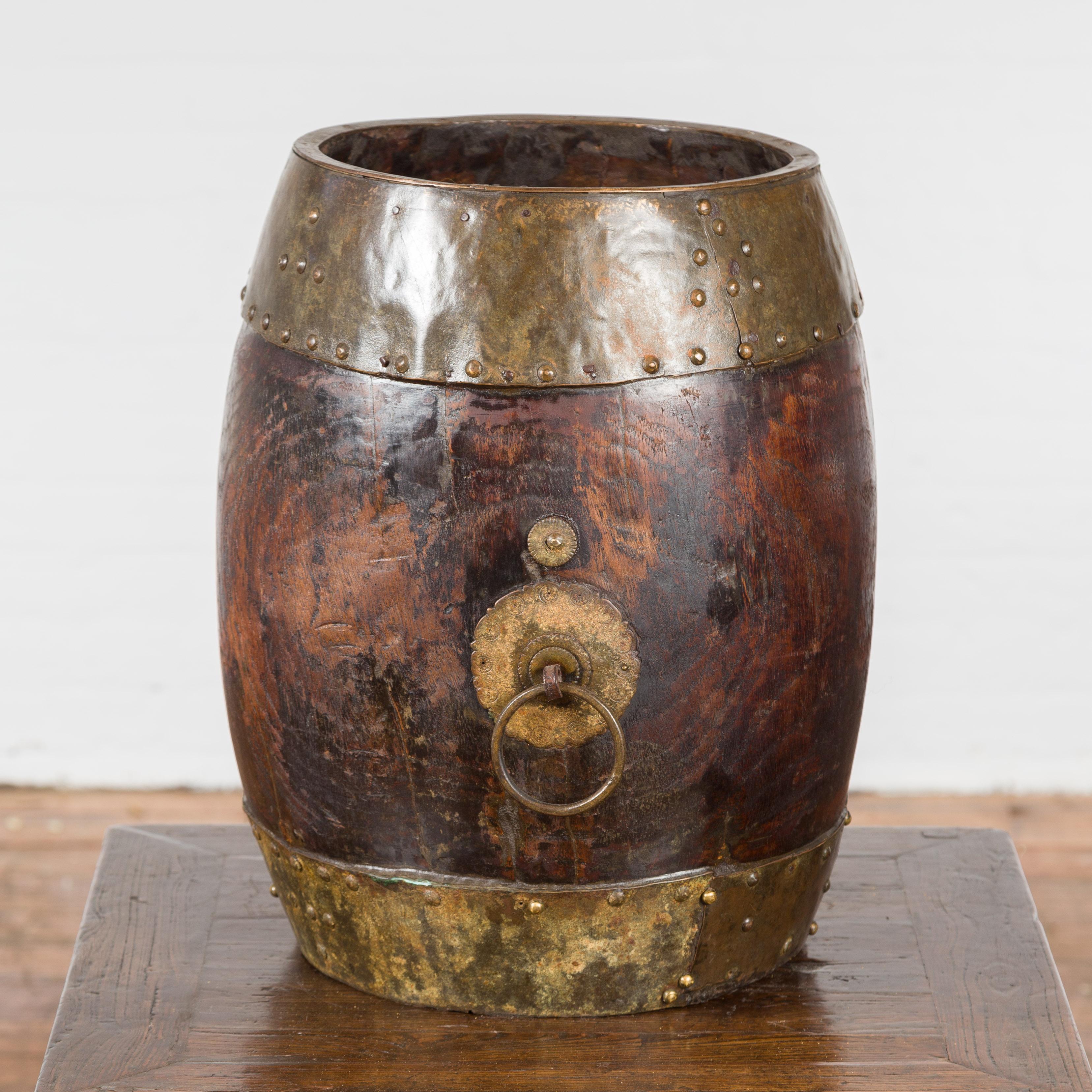 A Chinese vintage wooden bucket from the mid 20th century, with brass accents. Created in China during the midcentury period, this vintage bucket features a circular dark brown wooden body adorned with brass details and studs. Mixing rustic with the