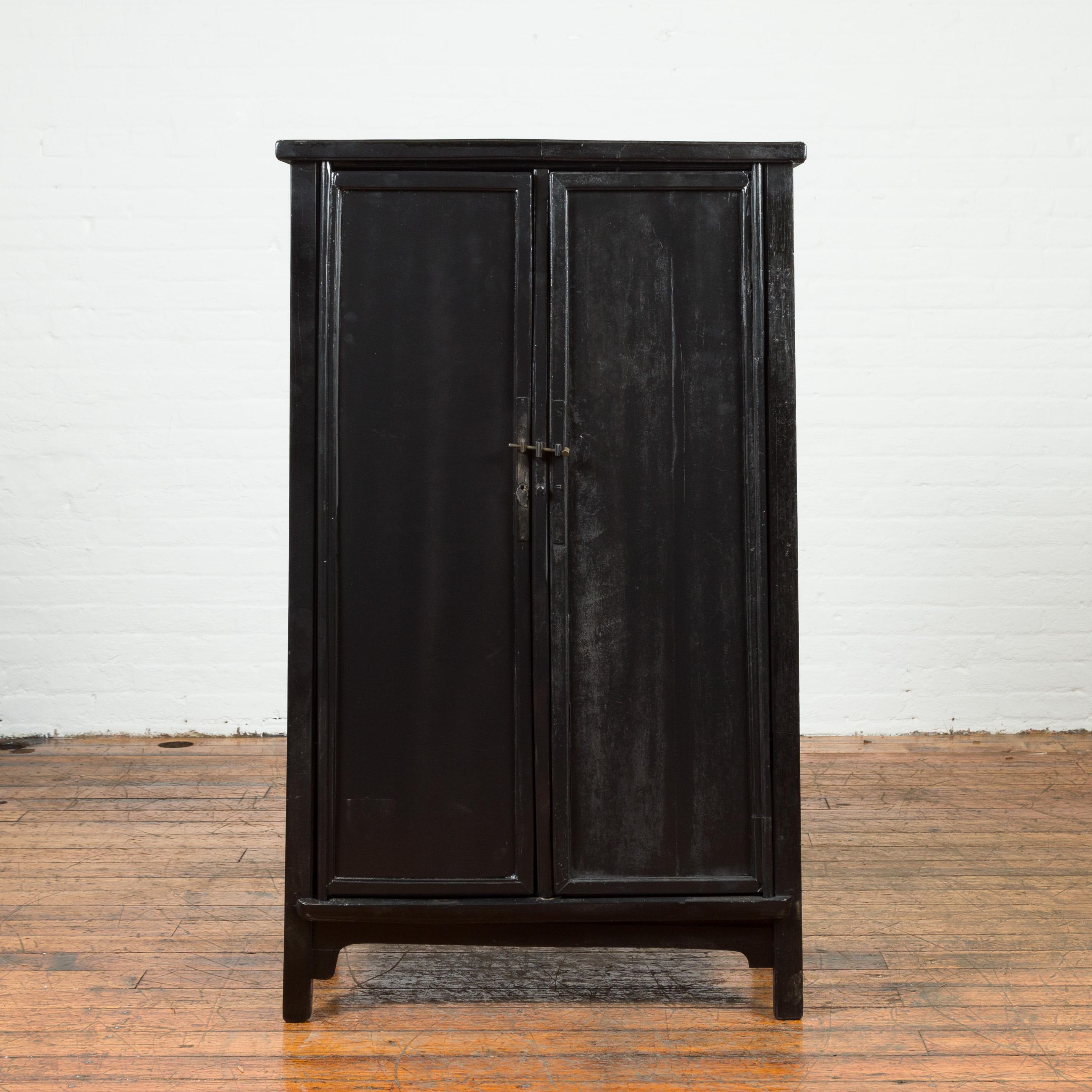 A Chinese vintage small cabinet from the mid 20th century, with tapered lines and black patina. Created in China during the midcentury period, this cabinet features a linear tapering silhouette perfectly complimented by a black patina. The façade is