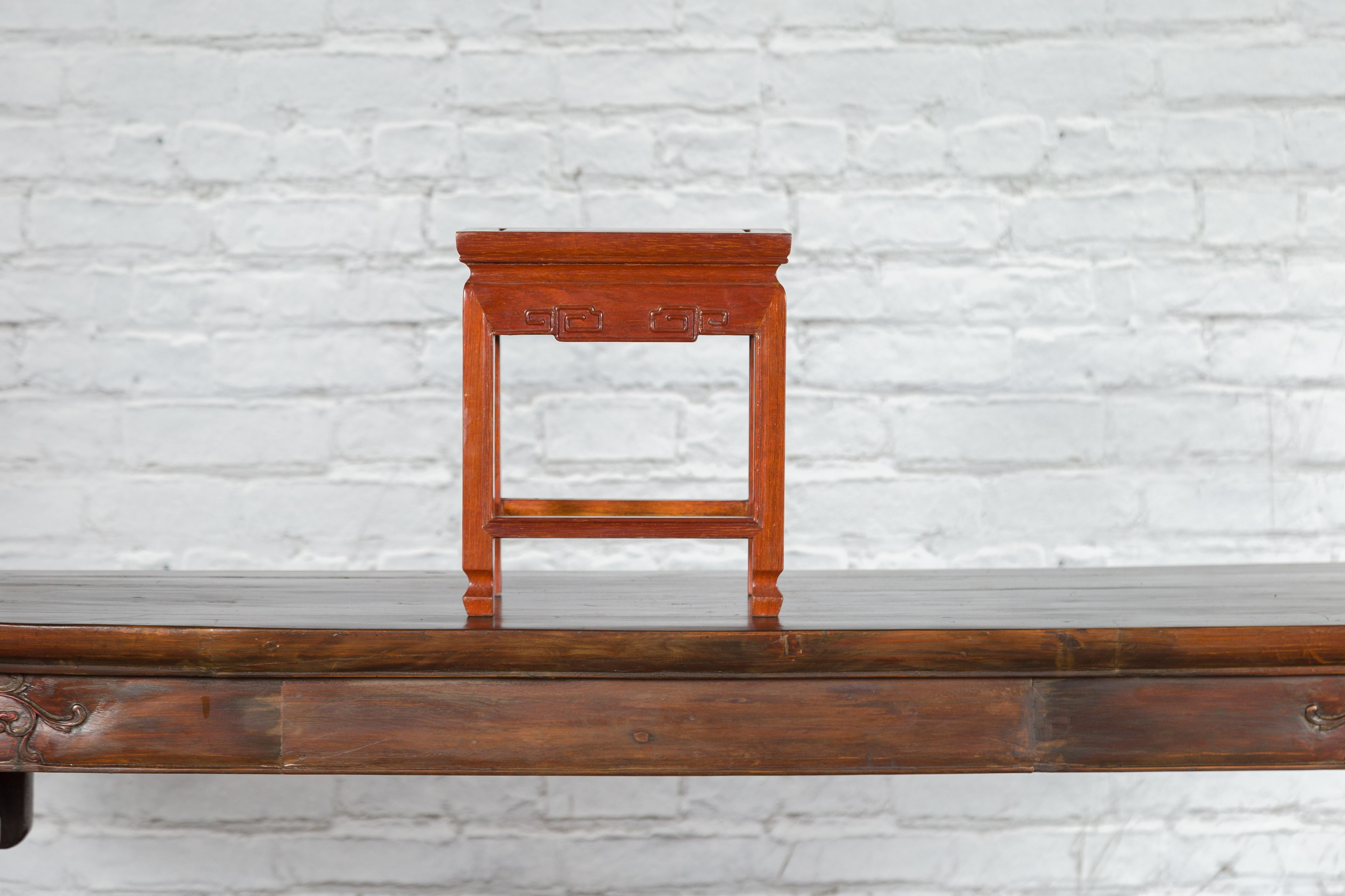 A vintage Chinese lacquered wood stool from the mid 20th century, with carved apron and side stretchers. Created in China during the midcentury period, this small lacquered stool features a rectangular top with central board, sitting above an