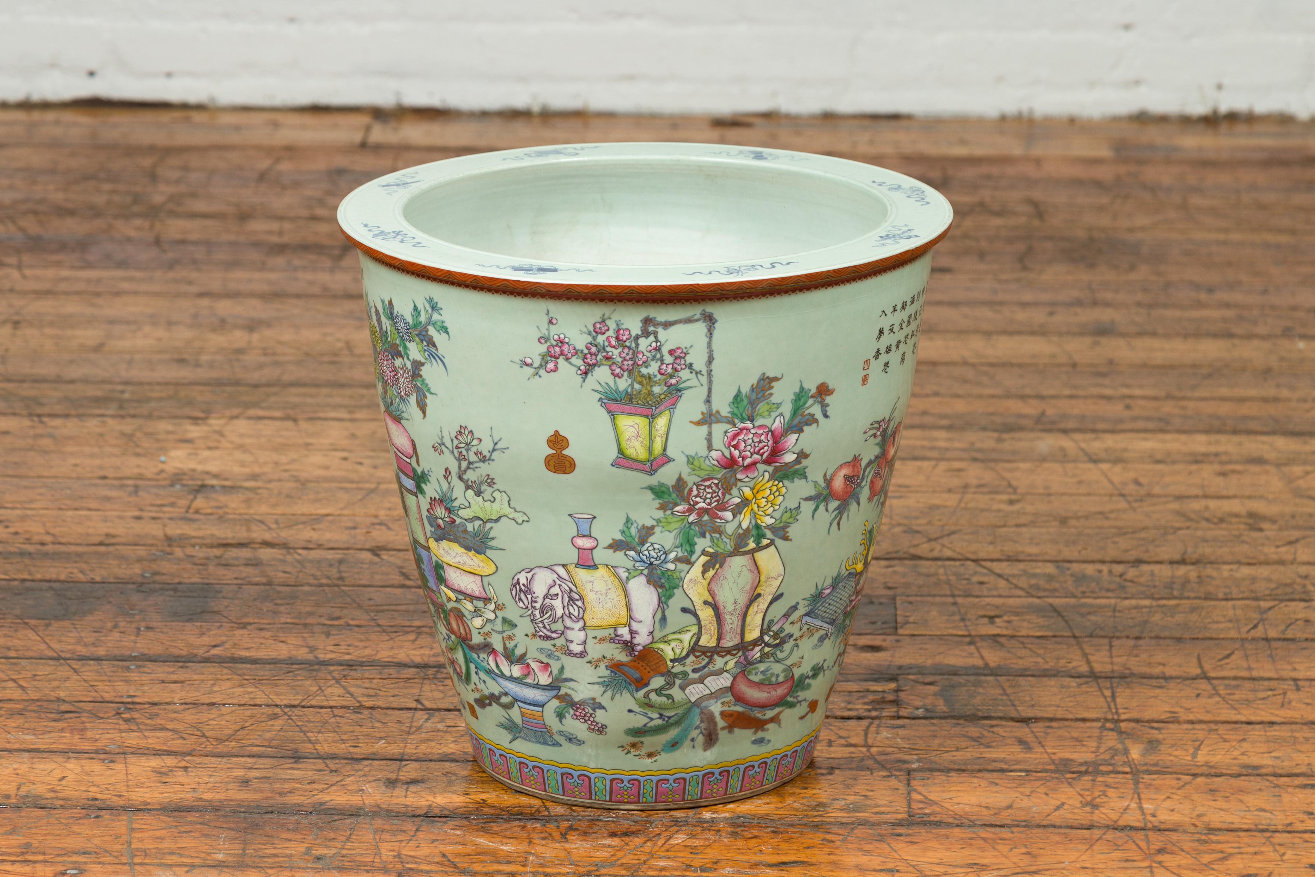 A Chinese vintage hand painted vase from the mid-20th century, with elephants, flowers, scholar's objects and fans. Created in China during the midcentury period, this large vase features a soft green ground adorned with a hand painted decor