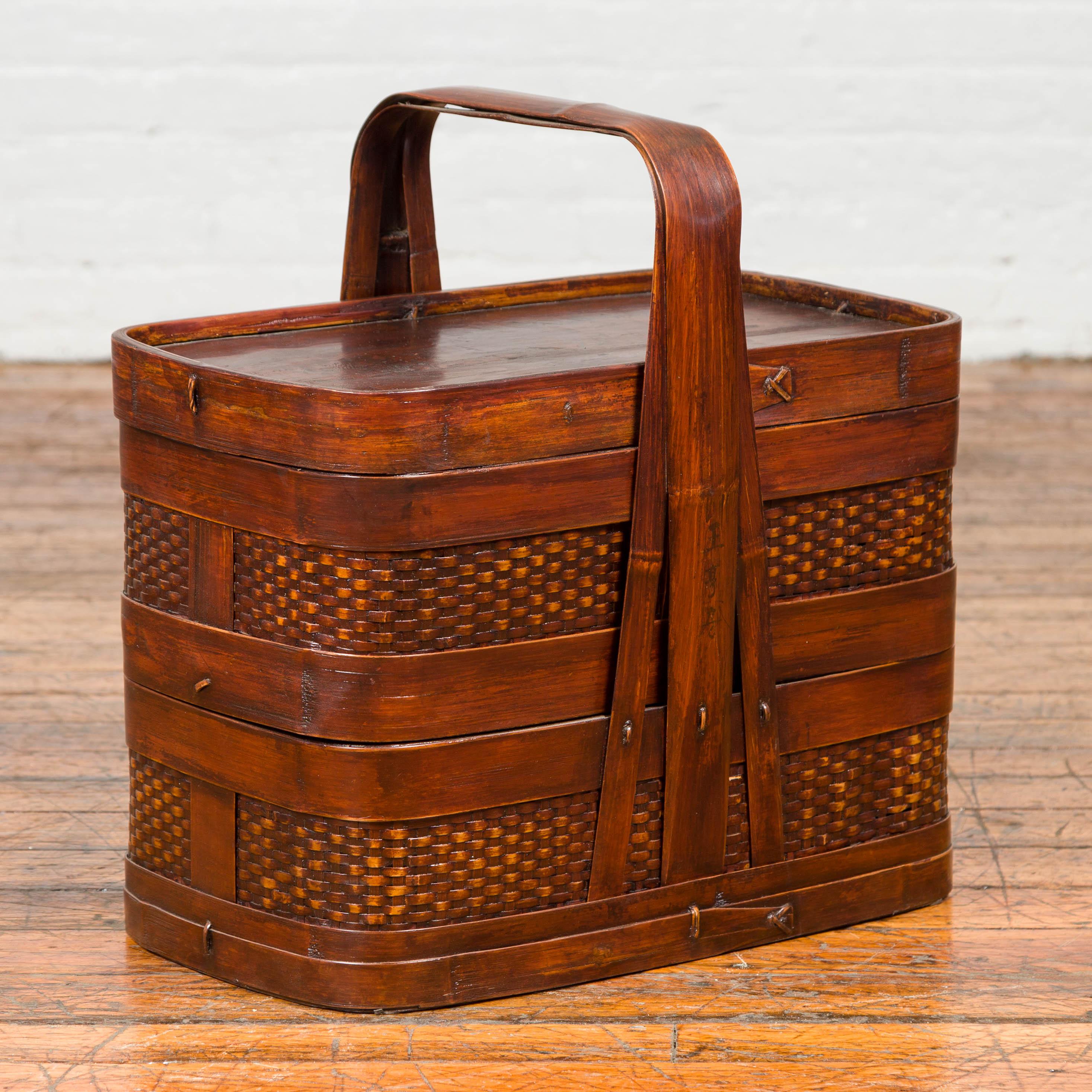 A Chinese vintage two-tier rattan and bamboo lunch basket from the mid-20th century, with large handle and lid. Born in China during the midcentury period, this lunch basket features two independent compartments topped with a rectangular lid.