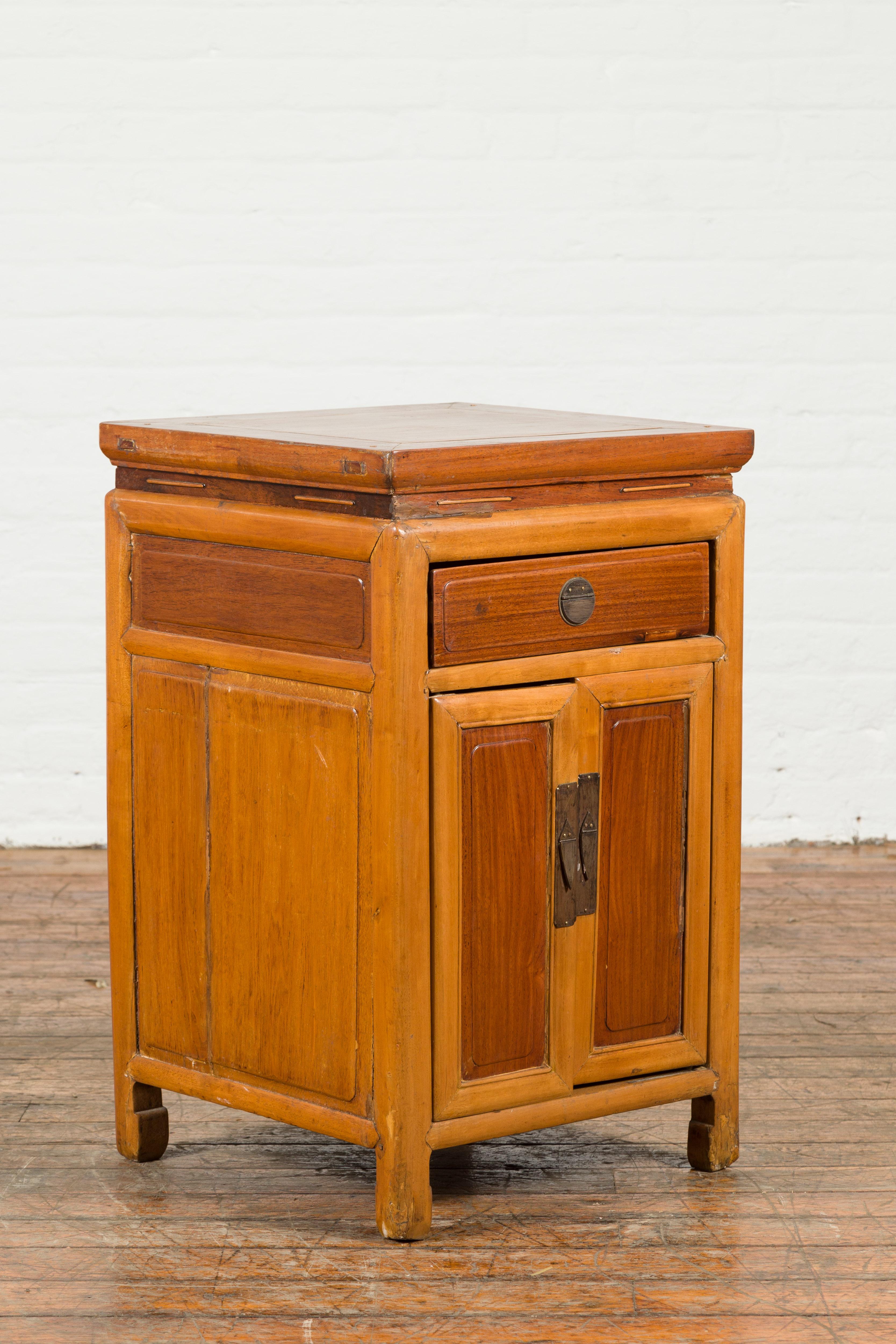 A Chinese vintage two-toned side table from the mid 20th century, with natural patina, single drawer and double doors. Created in China during the midcentury period, this vintage side table features a square waisted top with central board, sitting