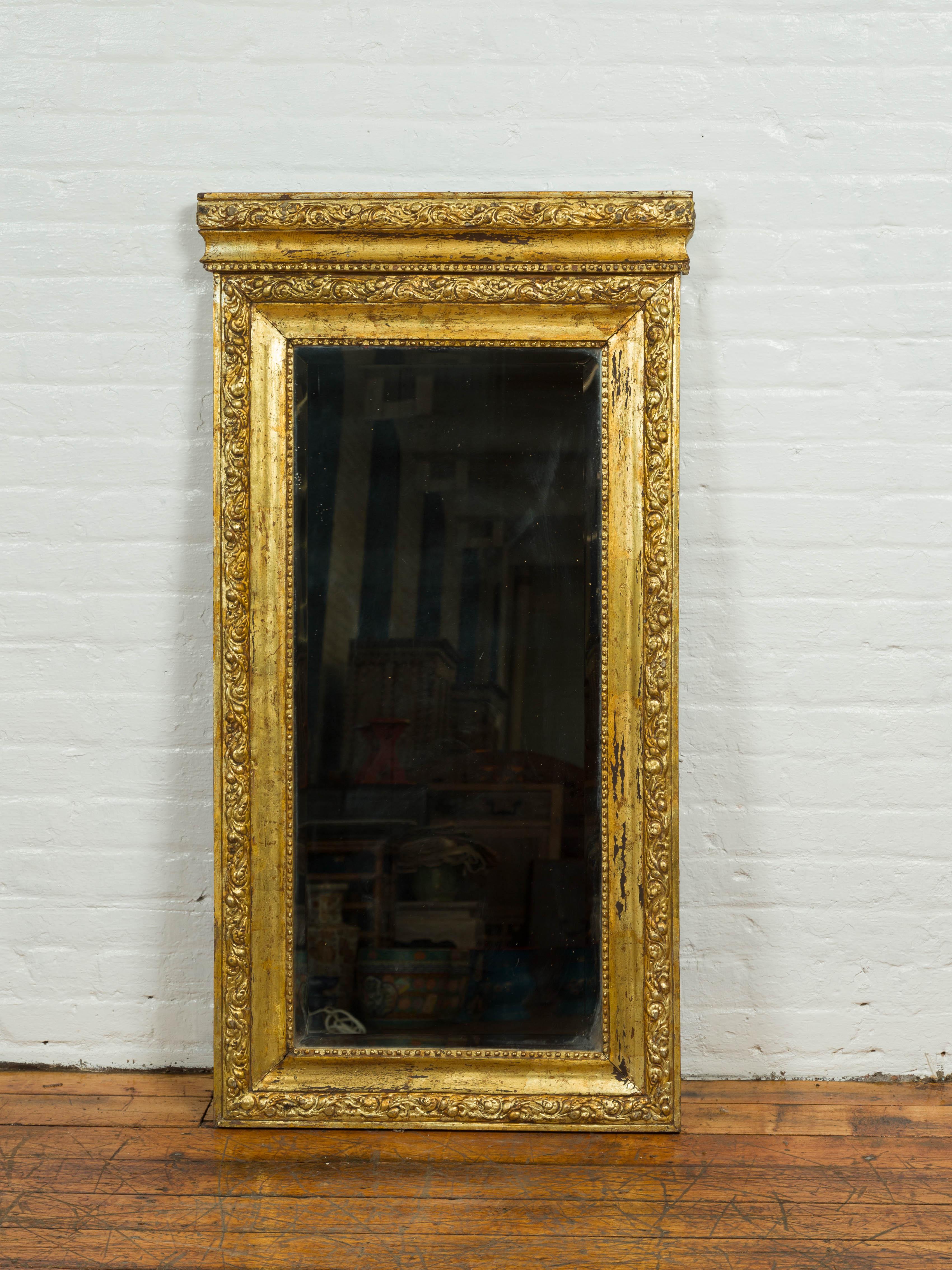 A vintage Chinese vertical giltwood mirror from the mid-20th century, with scrolling foliage and petite beads. Born in China during the midcentury period, this tall and narrow mirror features a giltwood frame topped with a carved cornice and cavetto