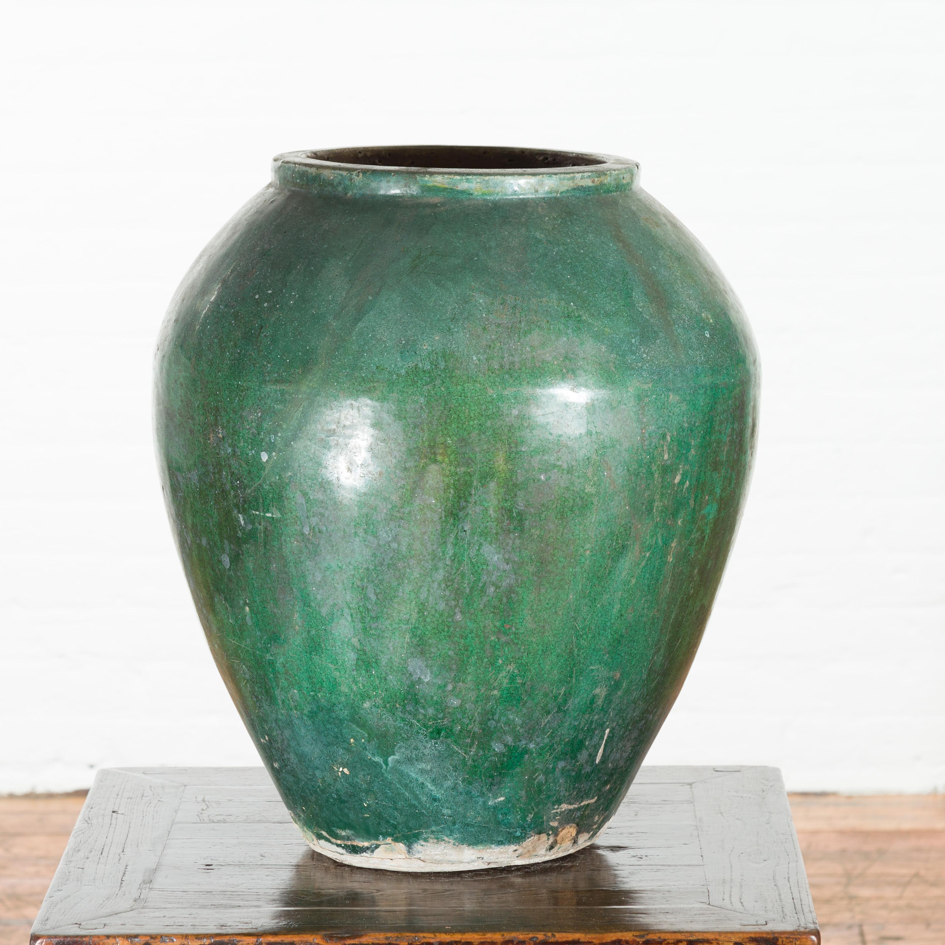 A Chinese vintage water jar from the mid 20th century, with verde patina. Created in China during the midcentury period, this green glazed water jar features a tapering body with nicely weathered appearance, topped with a lip surrounding an opening