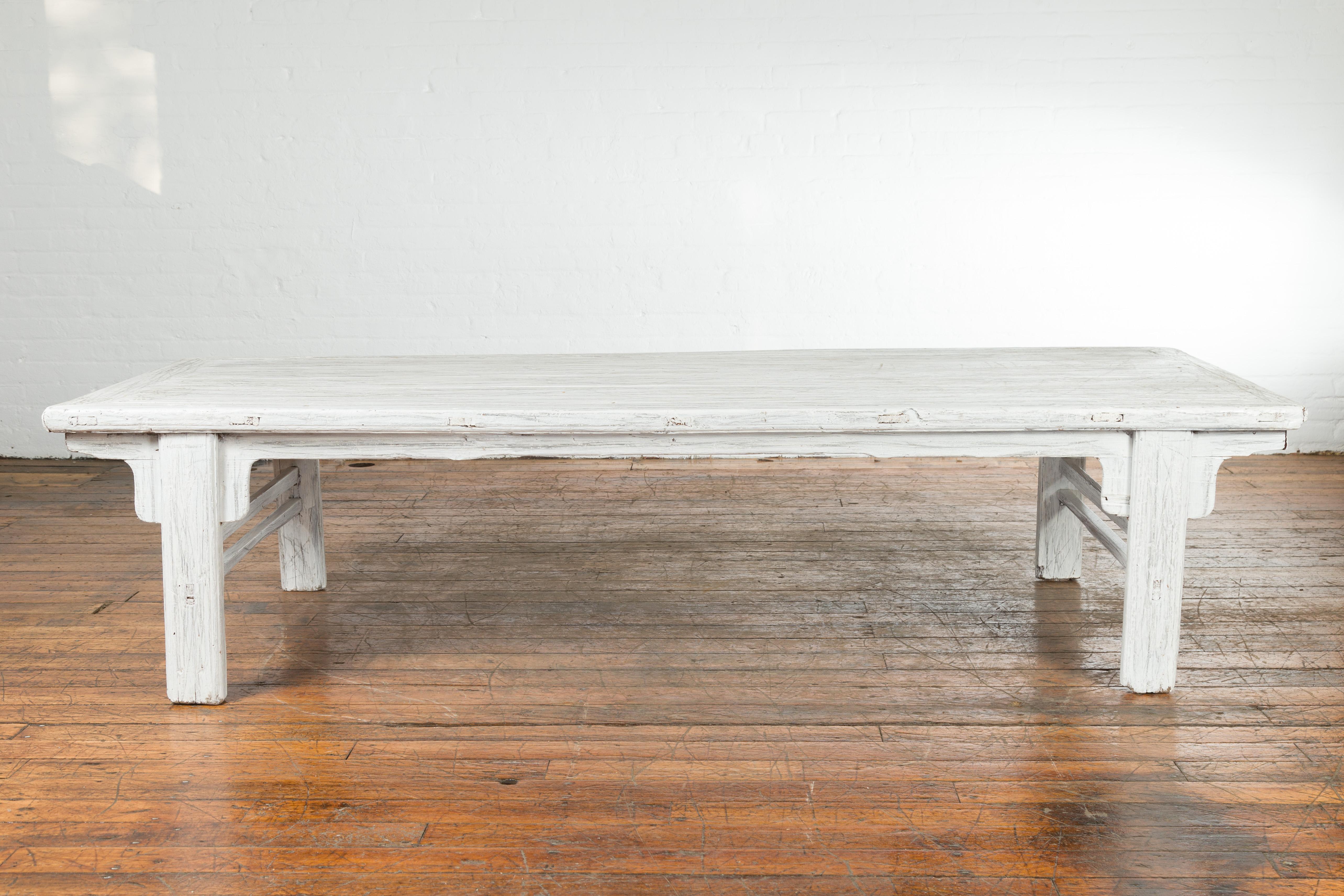 A Chinese vintage whitewashed coffee table from the mid 20th century, with carved spandrels and distressed appearance. Created in China during the midcentury period, this coffee table features a rectangular planked top sitting above a simply carved