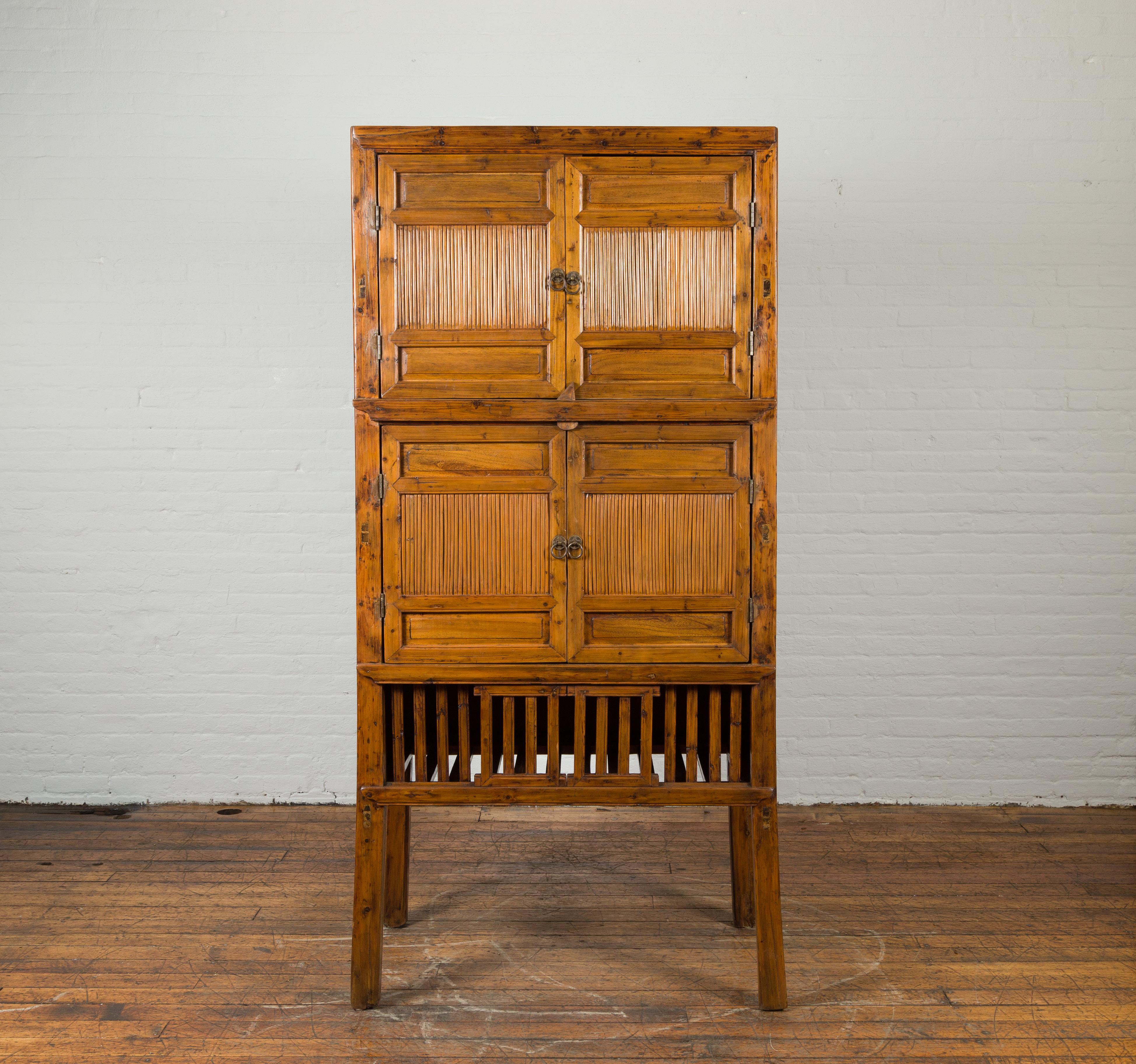 A Chinese vintage wood and bamboo cabinet from the mid 20th century, with double doors and openwork apron. Created in China during the midcentury period, this bamboo cabinet features two pairs of double doors alternating recessed panels and bamboo