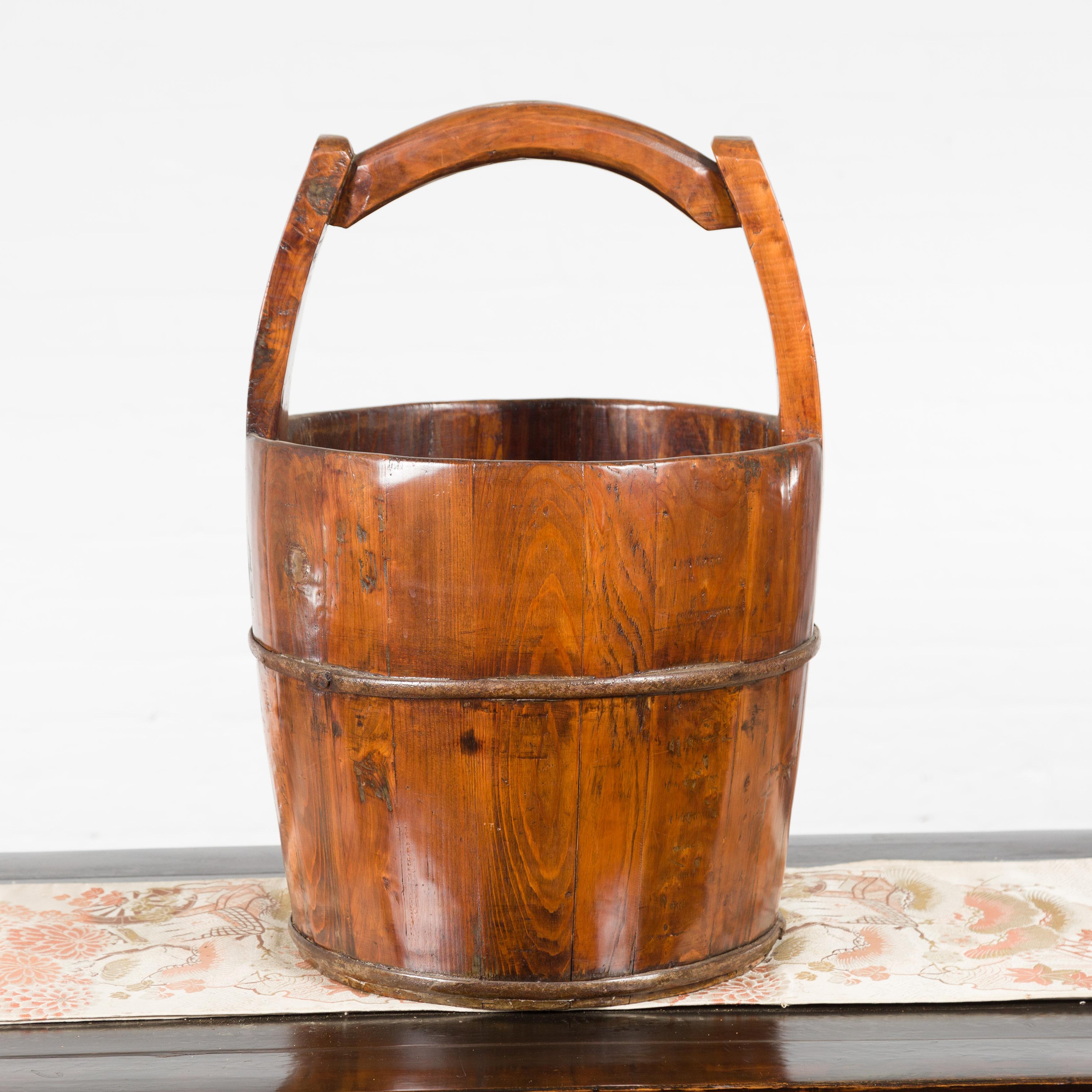 A Chinese vintage wooden grain basket from the mid 20th century, with large handle. Created in China during the midcentury period, this grain basket features a circular tapering body topped with a large handle and strengthened with a horizontal