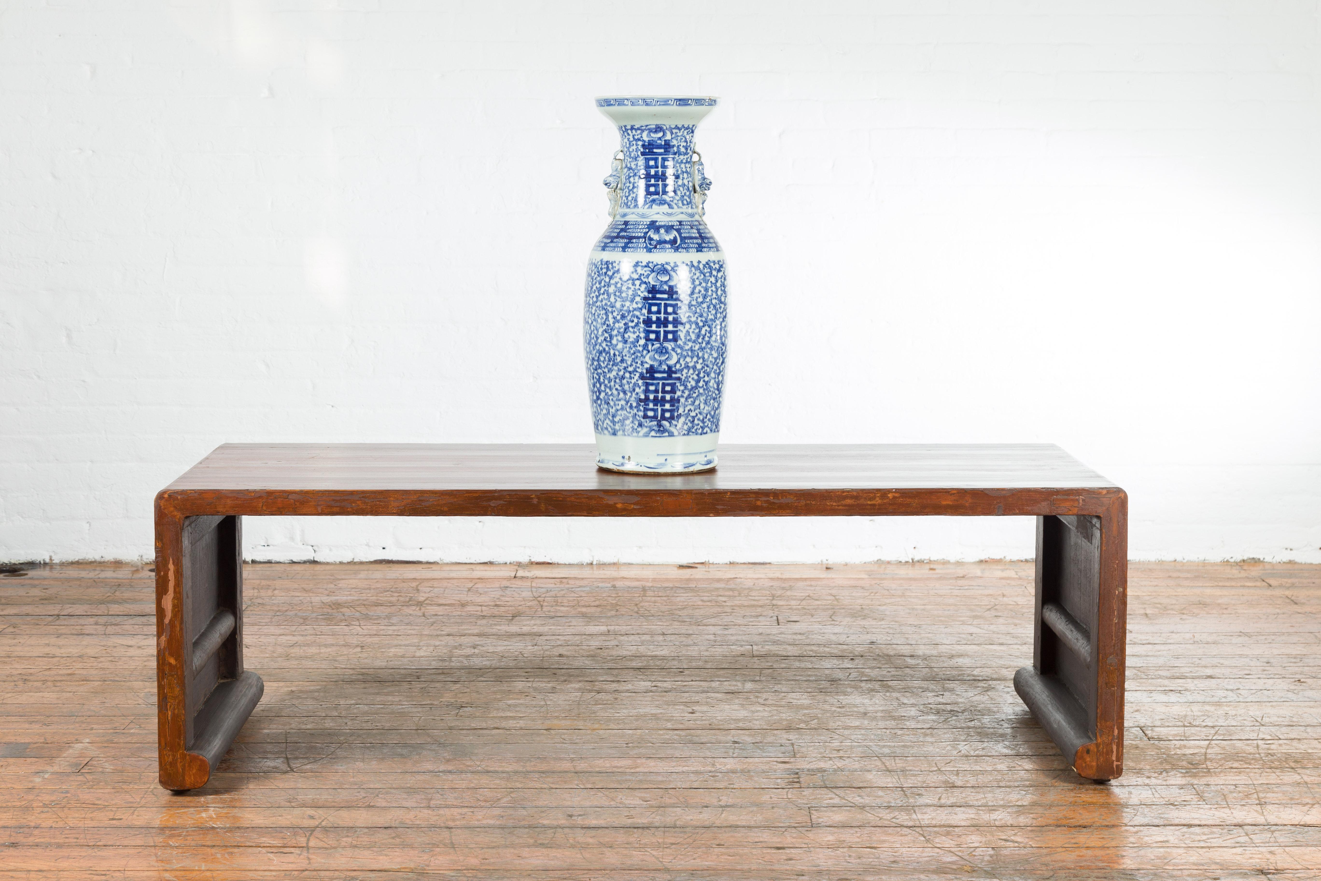 A Chinese vintage wooden waterfall coffee table from the mid 20th century, with scrolling extremities. Created in China during the midcentury period, this waterfall table features a rectangular top raised on solid board legs with scrolling accents.