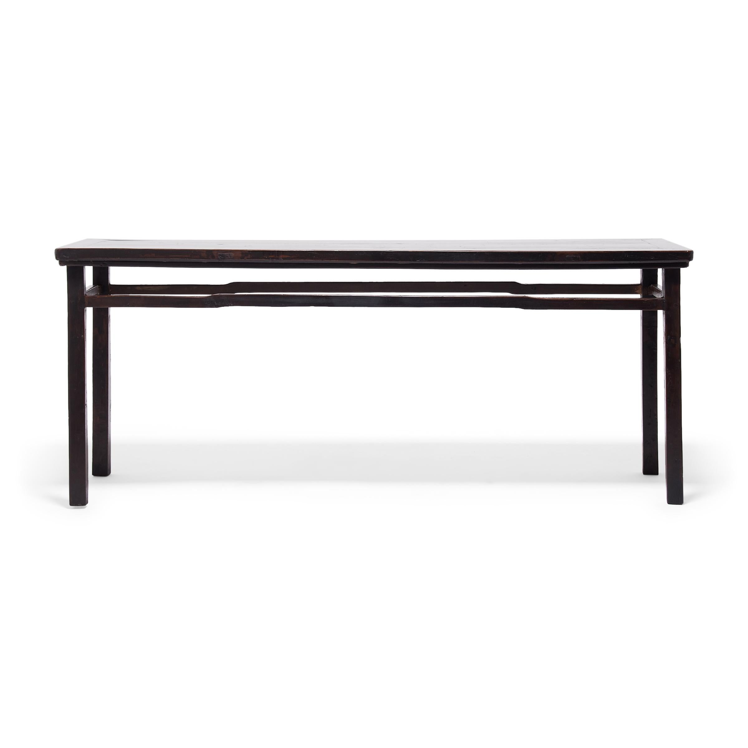Dated to the early 20th century, this long table has a Minimalist appeal, with clean lines and a darkly lacquered finish. The walnut table exemplifies Classic Chinese furniture design and features an expansive floating-panel top, squared legs, and