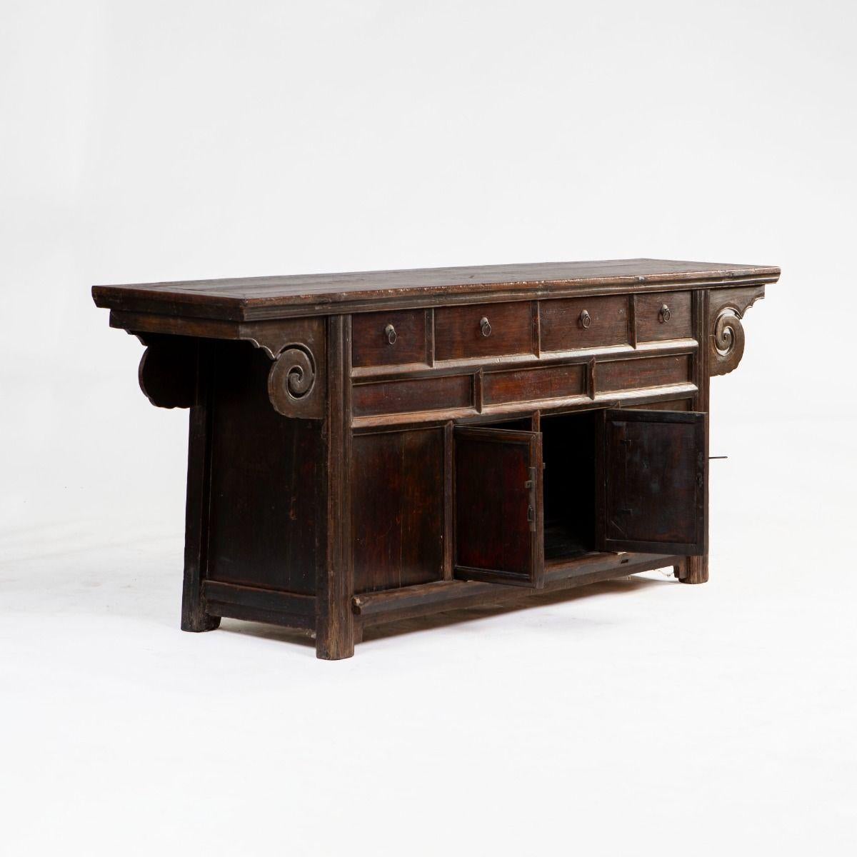 Buffet en noyer composé de quatre tiroirs et d'une paire de portes à double battant.
Les côtés sont ornés de détails sculptés en forme de volutes.
Fabriquée par des experts, la pièce conserve des traces de sa laque bordeaux foncé d'origine et a