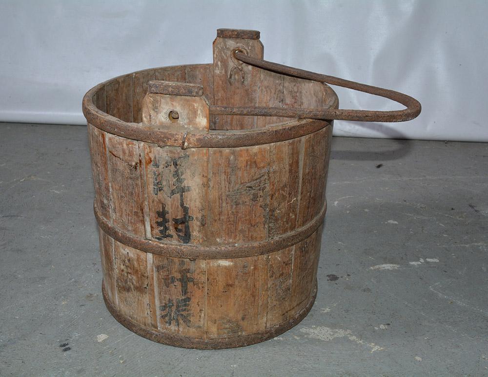 A classically shaped antique Chinese cypress water bucket with original cast iron handles and straps. Nicely worn. An historical piece with Chinese calligraphy. The bucket has many practical uses including, firewood storage, magazine or book