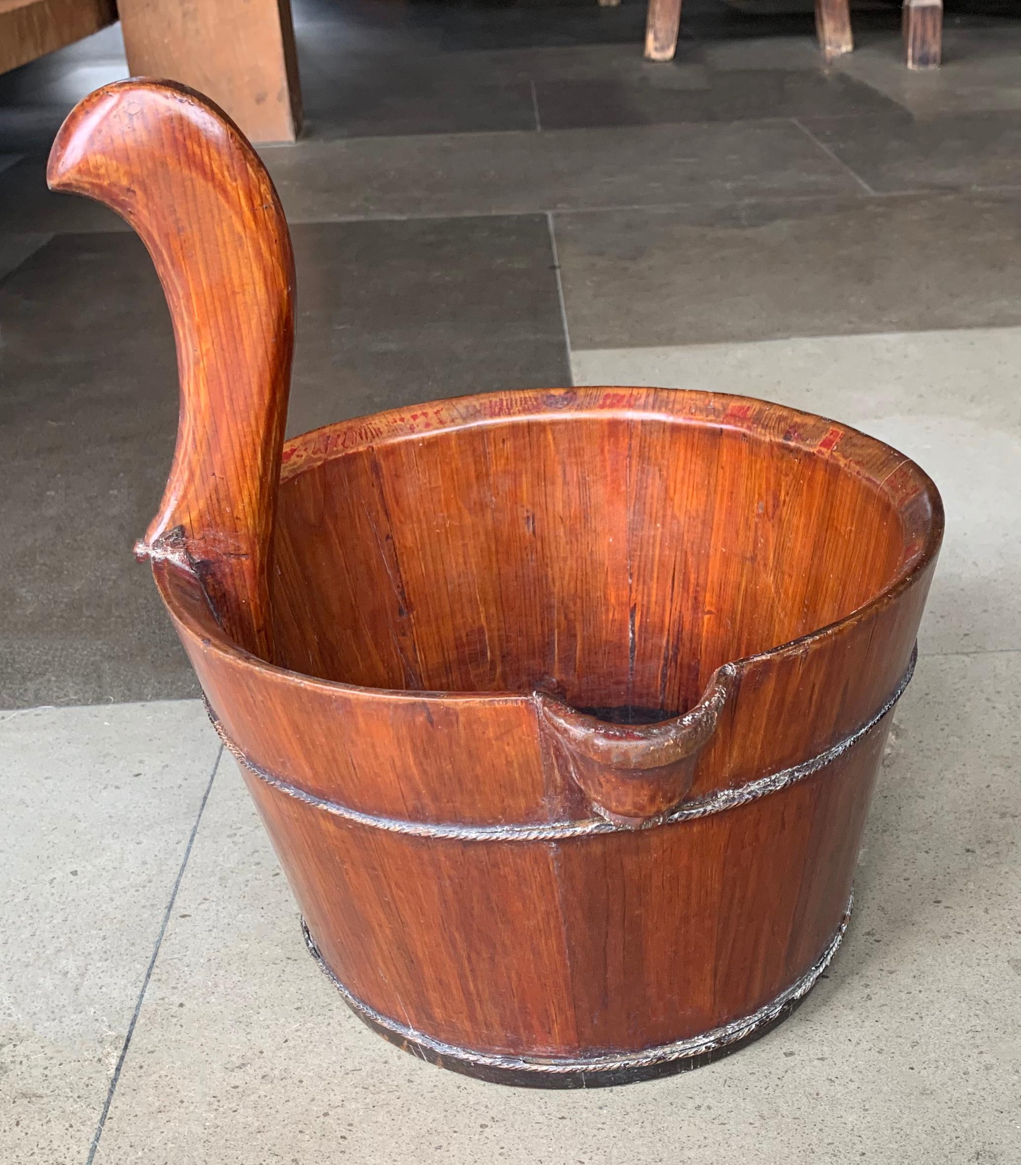 Este cubo de agua chino de madera está hecho a mano con pequeños paneles de madera que se mantienen unidos por bandas de metal entretejido. También tiene un mango curvado. 

Dimensiones; Altura hasta el mango 23 cm x altura 18 cm x diámetro 27,5