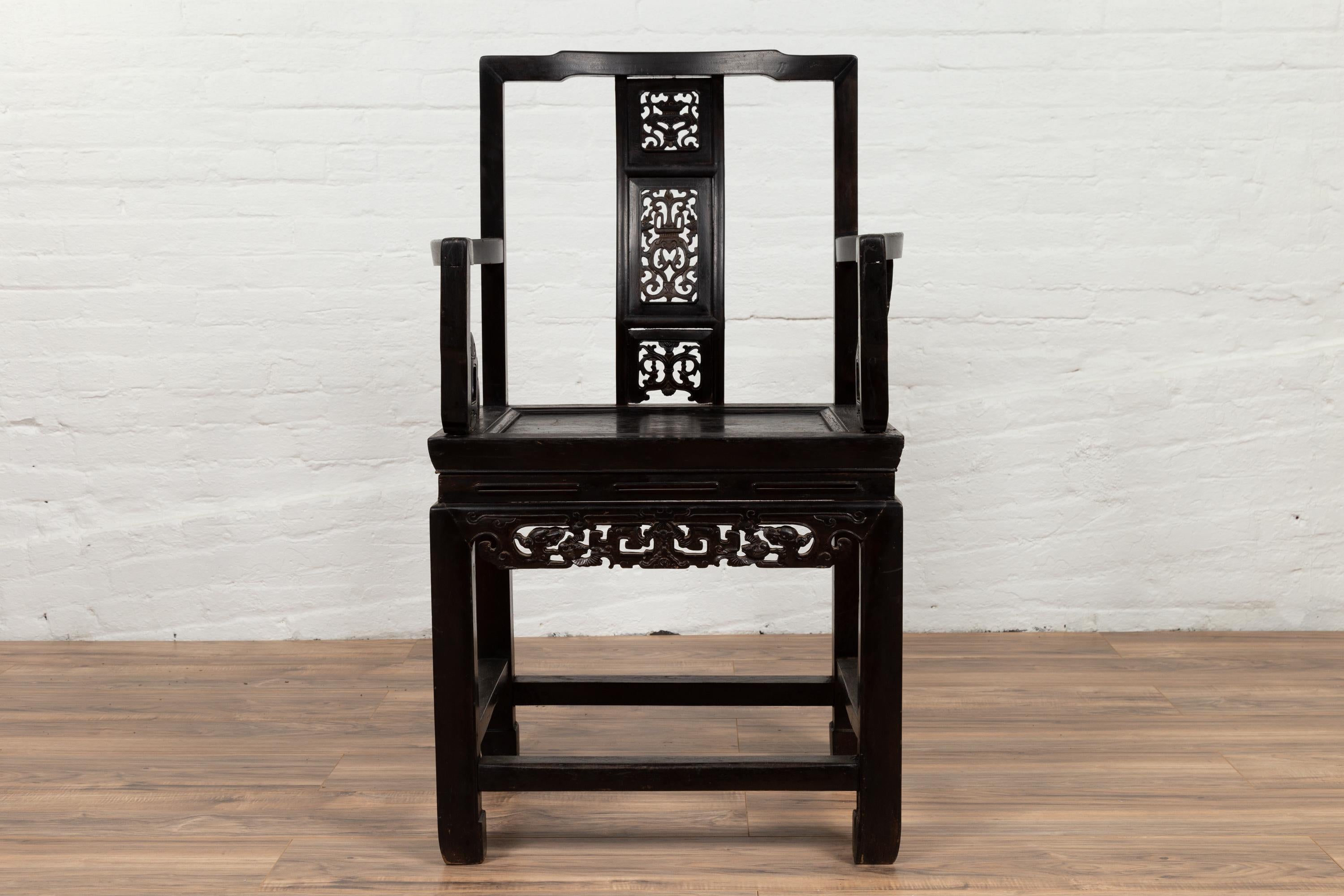 A Chinese antique wedding chair from the early 20th century, with black patina and carved motifs. Born in China during the early years of the 20th century, this exquisite wedding chair features an open straight back, adorned with a sinuous central