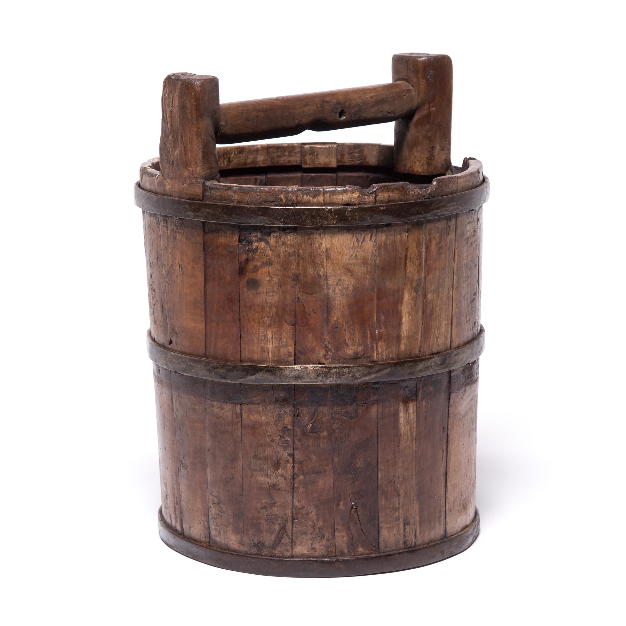 This vintage water bucket conjures up images of water-bearing figures illustrated in painted scrolls. Beautifully aged with a warm patina, this Qing-dynasty bucket draws attention to the ingenuity of its manufacture, consisting of staves of cypress