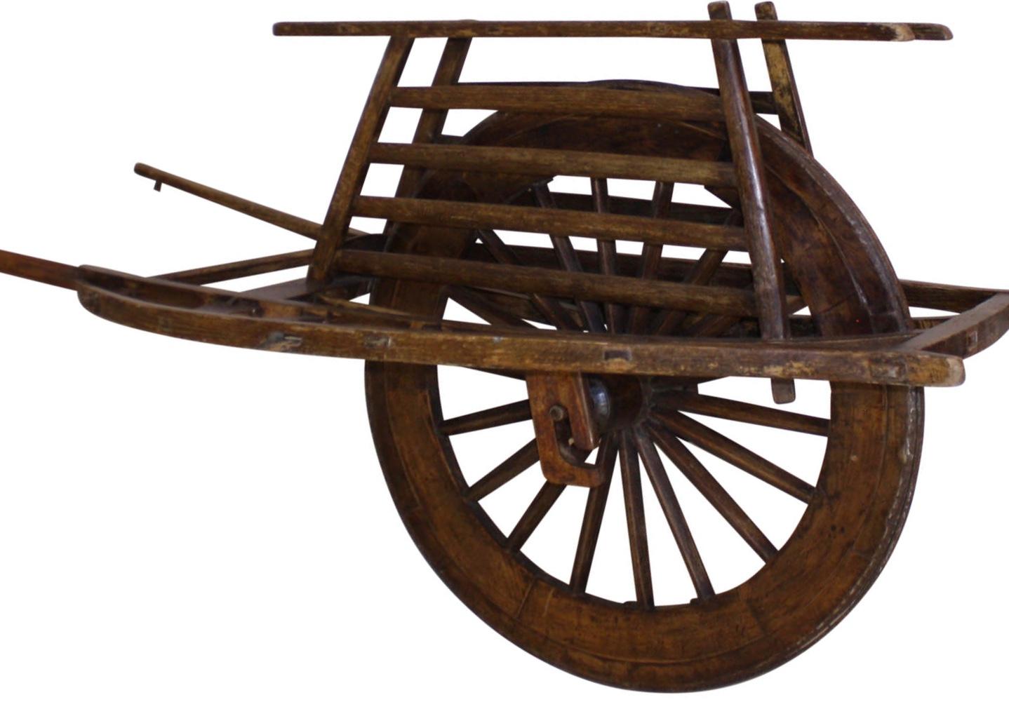 This wheelbarrow has a single, three-foot wheel with a carrying surface that encases the top of the wheel and is flanked by a platform on each side. The platform was designed for transporting supplies and people. The wheel's axle attaches to the