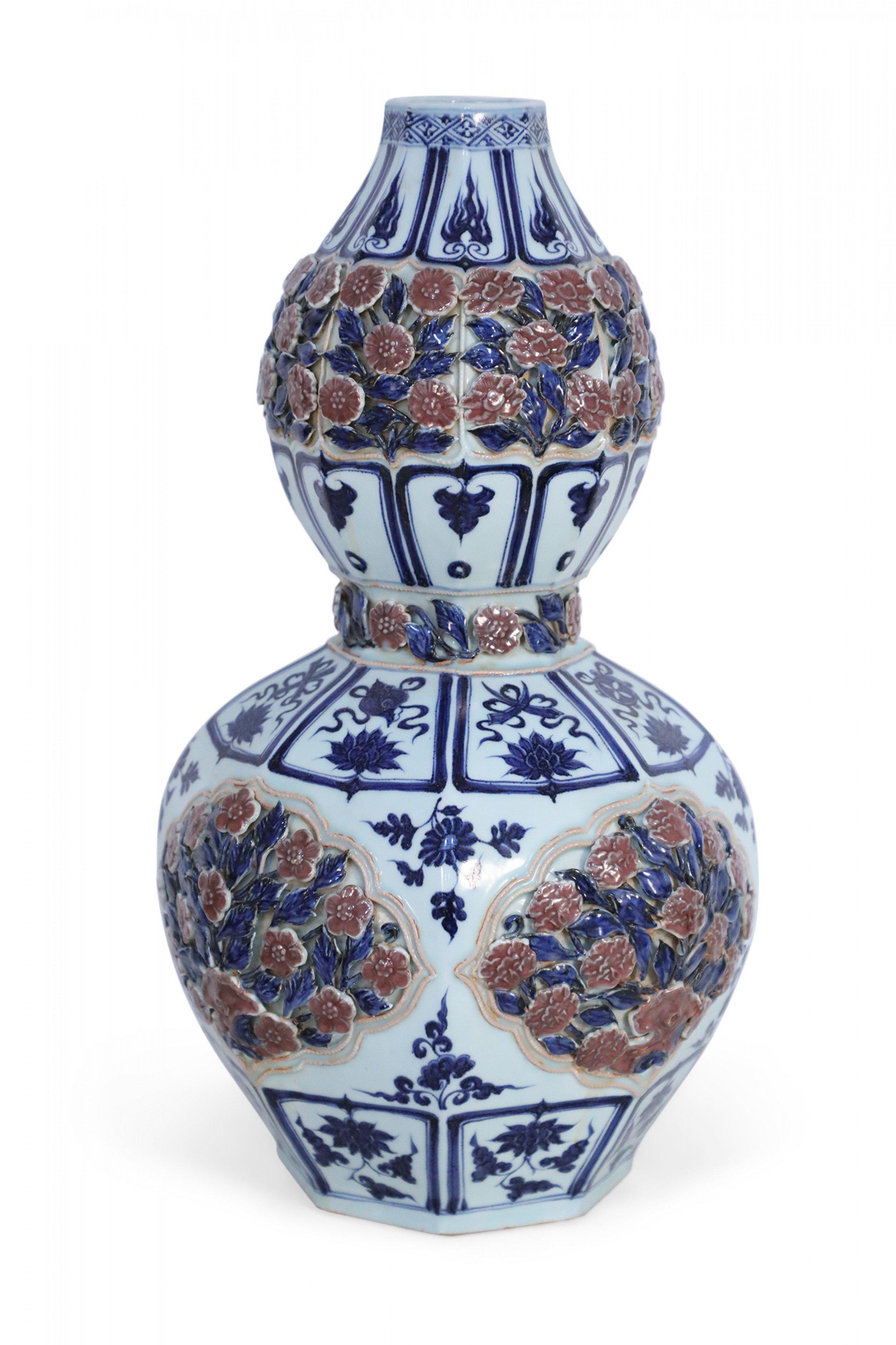 Chinese white and blue double-gourd porcelain vase decorated with bands of blue, framed iconography, and raised, pierced roses amid leaves wrapping the top and middle sections, and as the central motif around the bulbous bottom half.