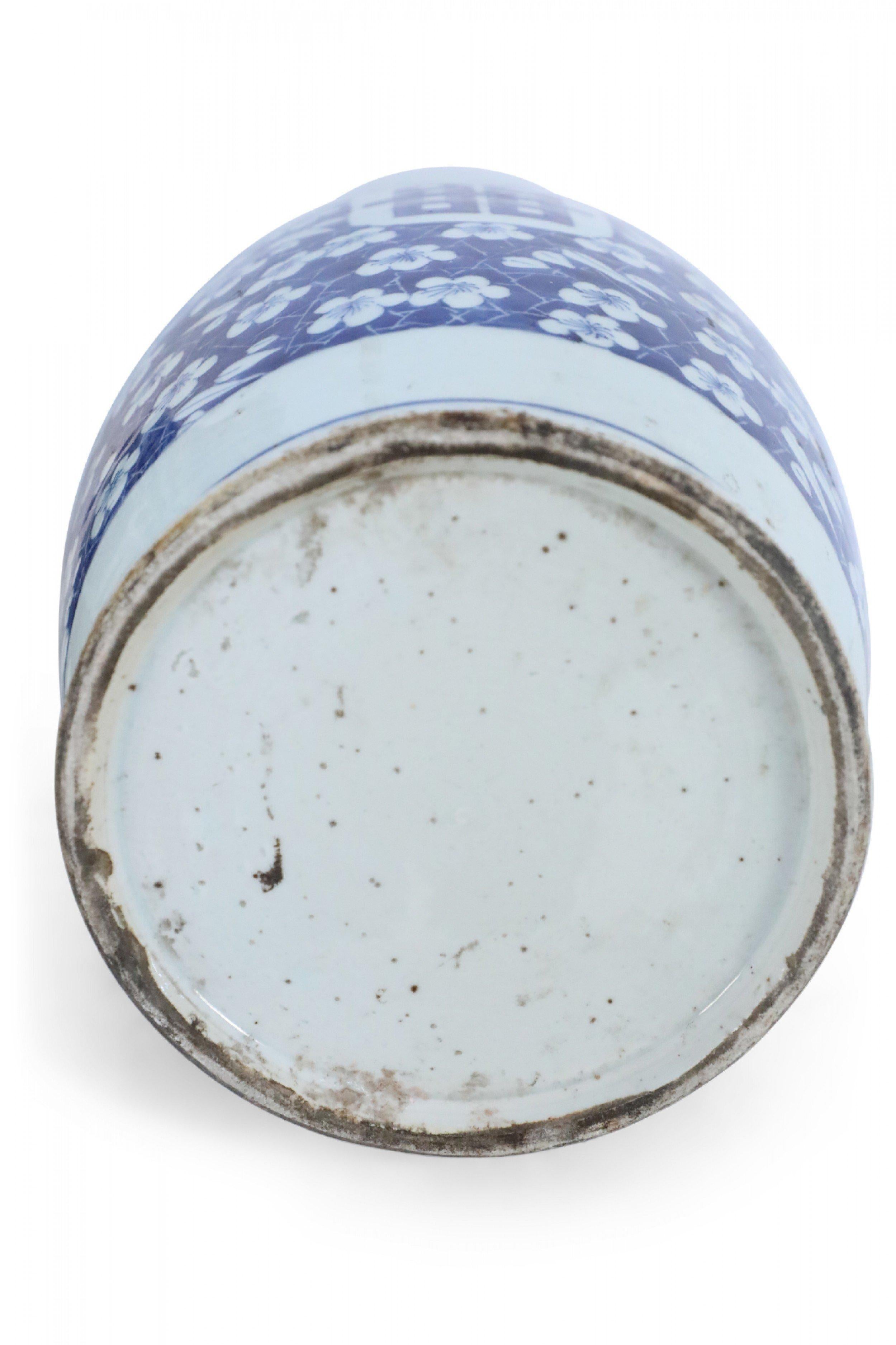Chinese porcelain urn painted with a blue and white floral background surrounding a center white oval with bold markings, dark blue feathers along the neck, and geometric patterned bands at the top, middle and base.
 