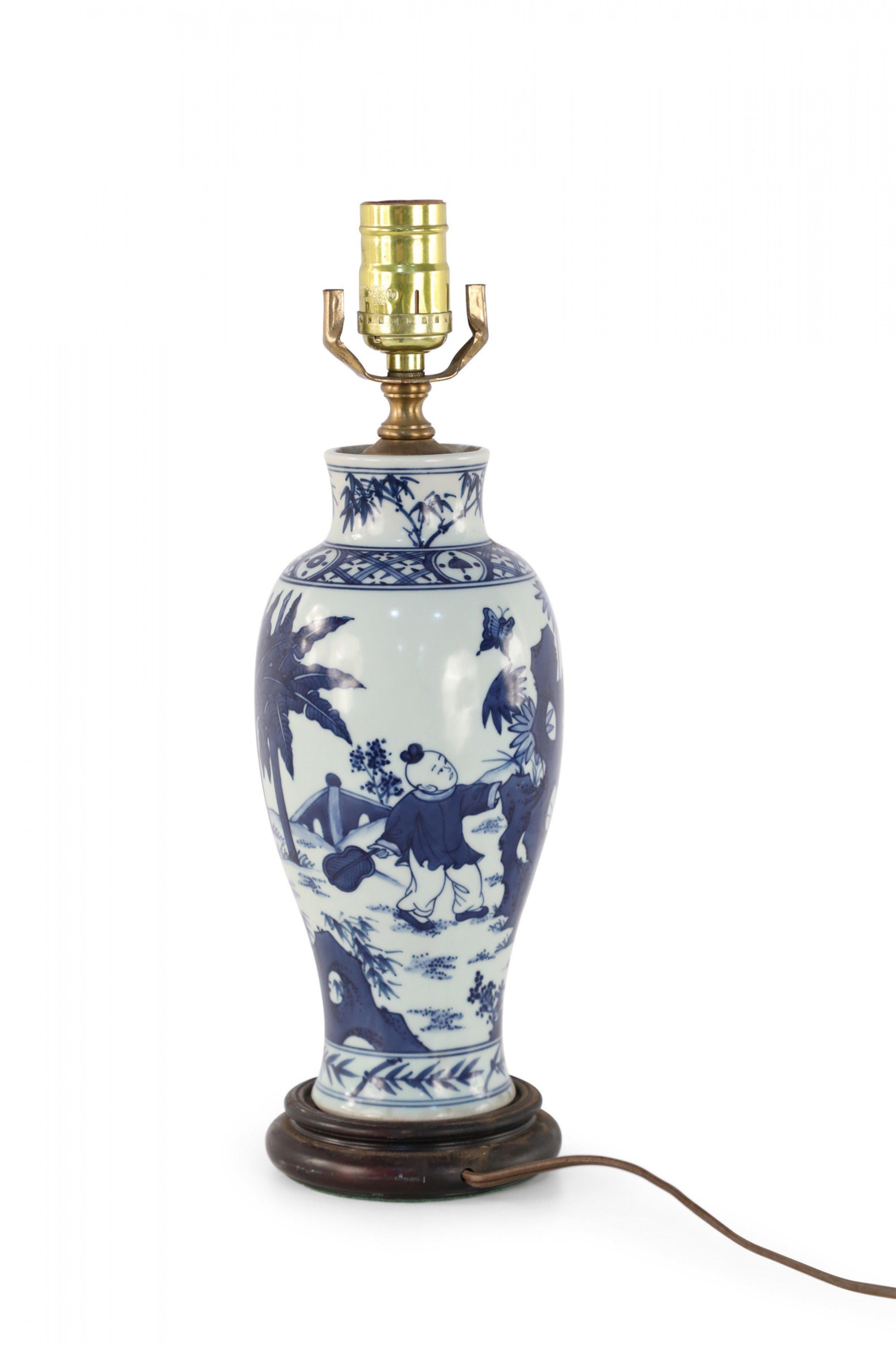 Antique Chinese (Early 20th Century) table lamp made from a white and blue baluster-shaped porcelain vase depicting a mother and children playing outside, mounted on a wooden base with brass hardware.
 