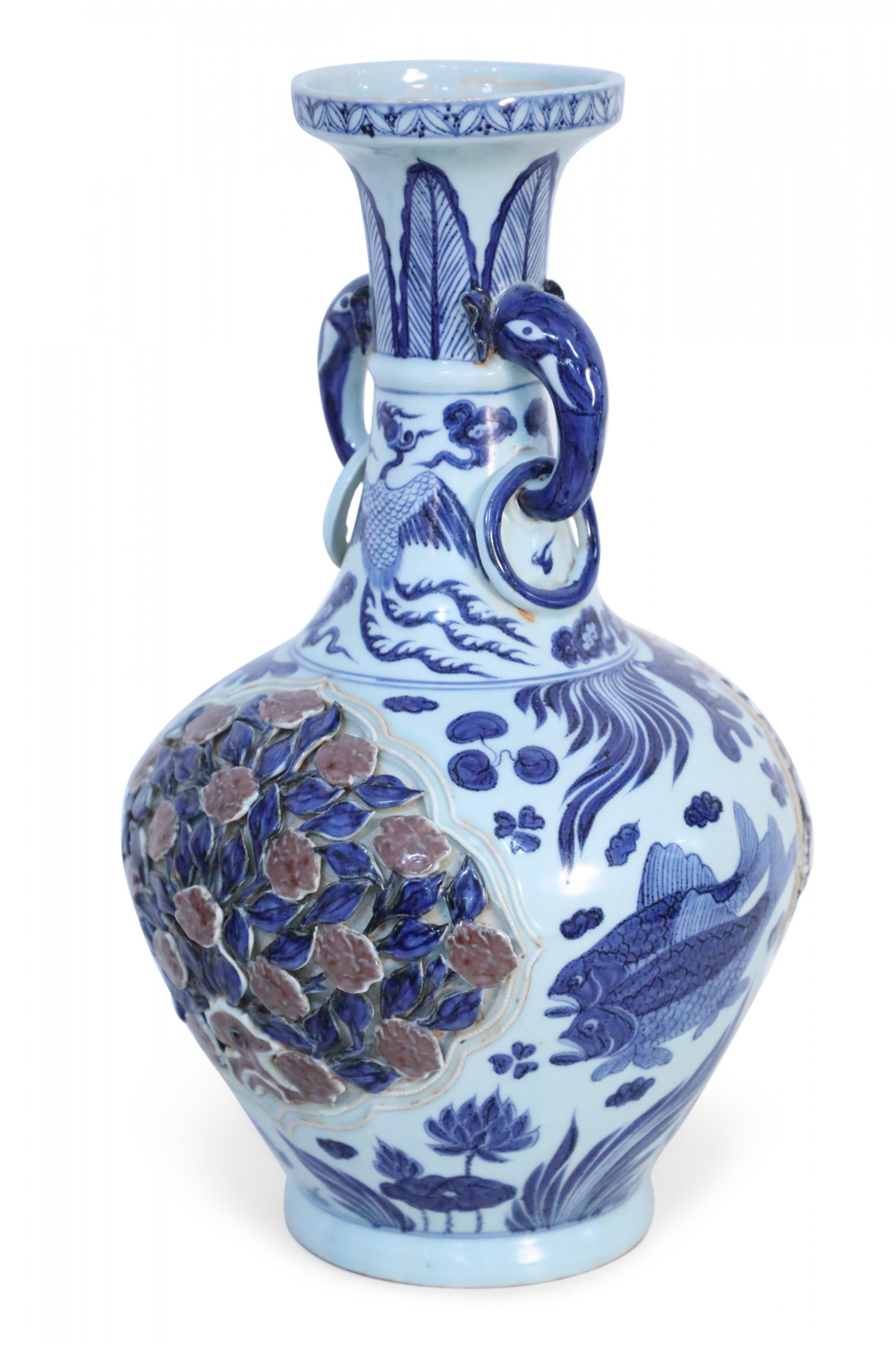 Chinese white porcelain vase with a bulbous body decorated in blue koi, cranes, clouds and vegetation, surrounding a central raised, pierced rose bush on each side. The thin neck features a band of blue feathers leading up the opening, and two