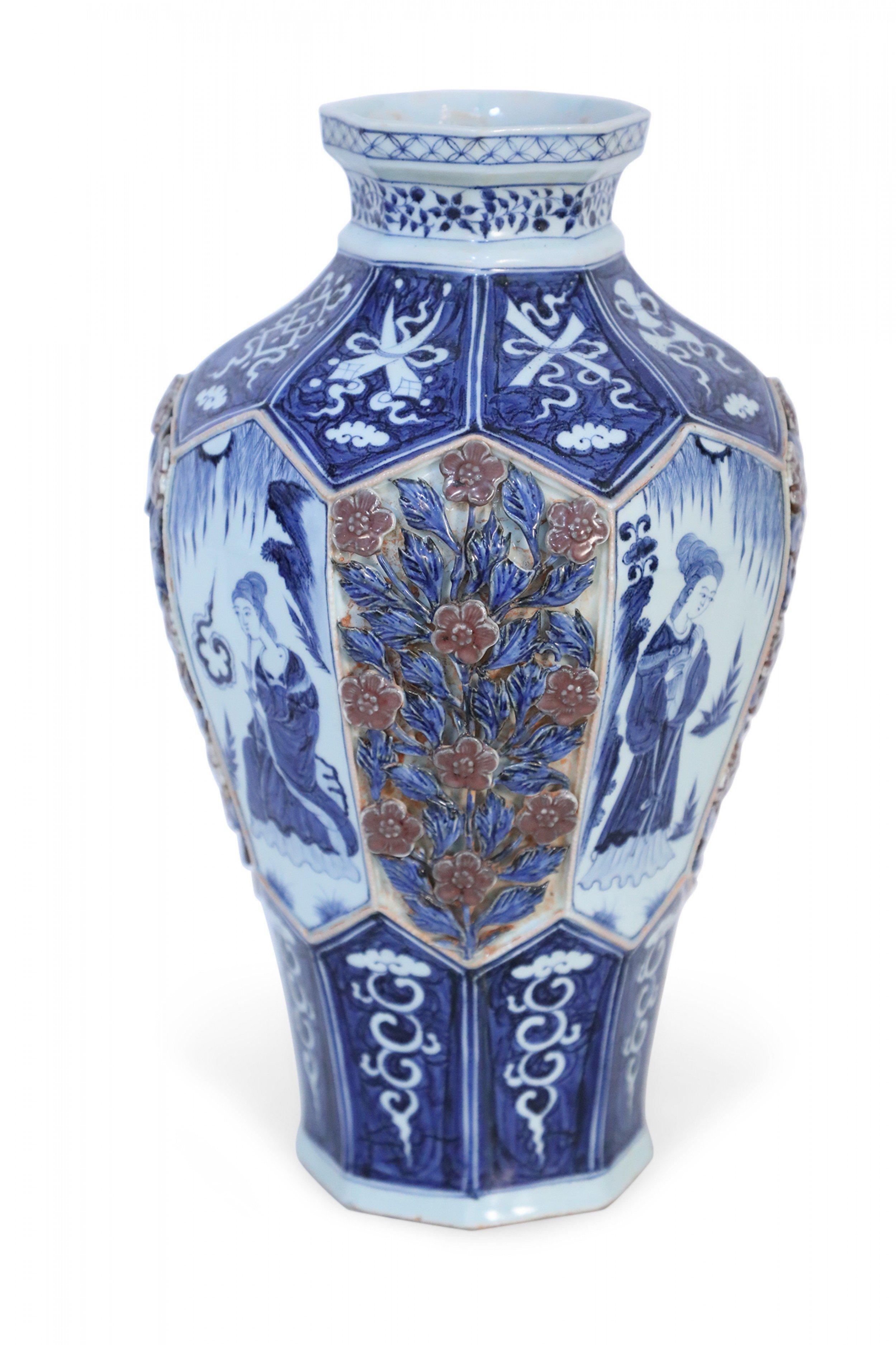 Chinese blue and white porcelain vase with an octagonal, faceted shape wrapped in blue bands featuring white iconography at the base and concave top, framing a center area that alternates figurative vignette panels with raised, pierced roses amid