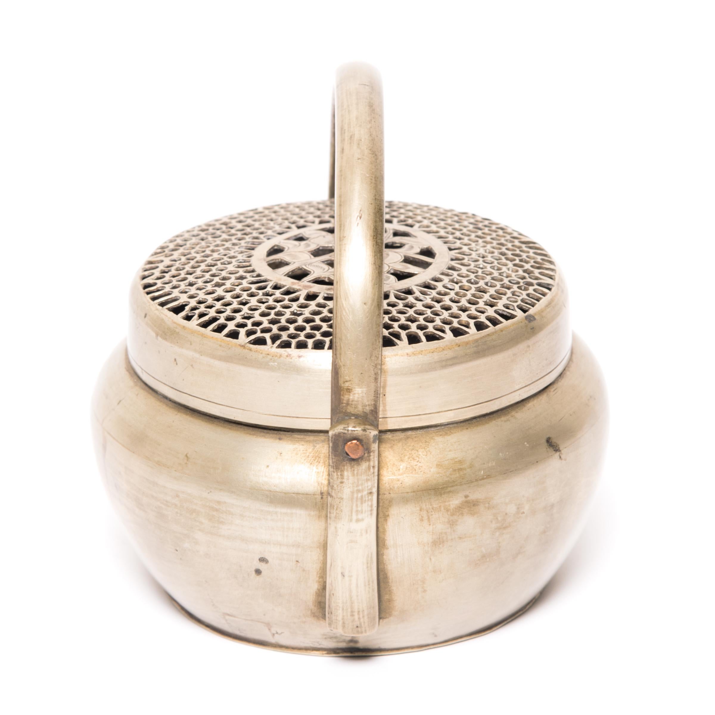 Filled with burning coals, this petite 19th-century brass brazier once warmed the hands of a well-to-do person on a cold winter's night in northern China. The round brazier is crafted of white brass with a hinged handle and a lid pierced with an