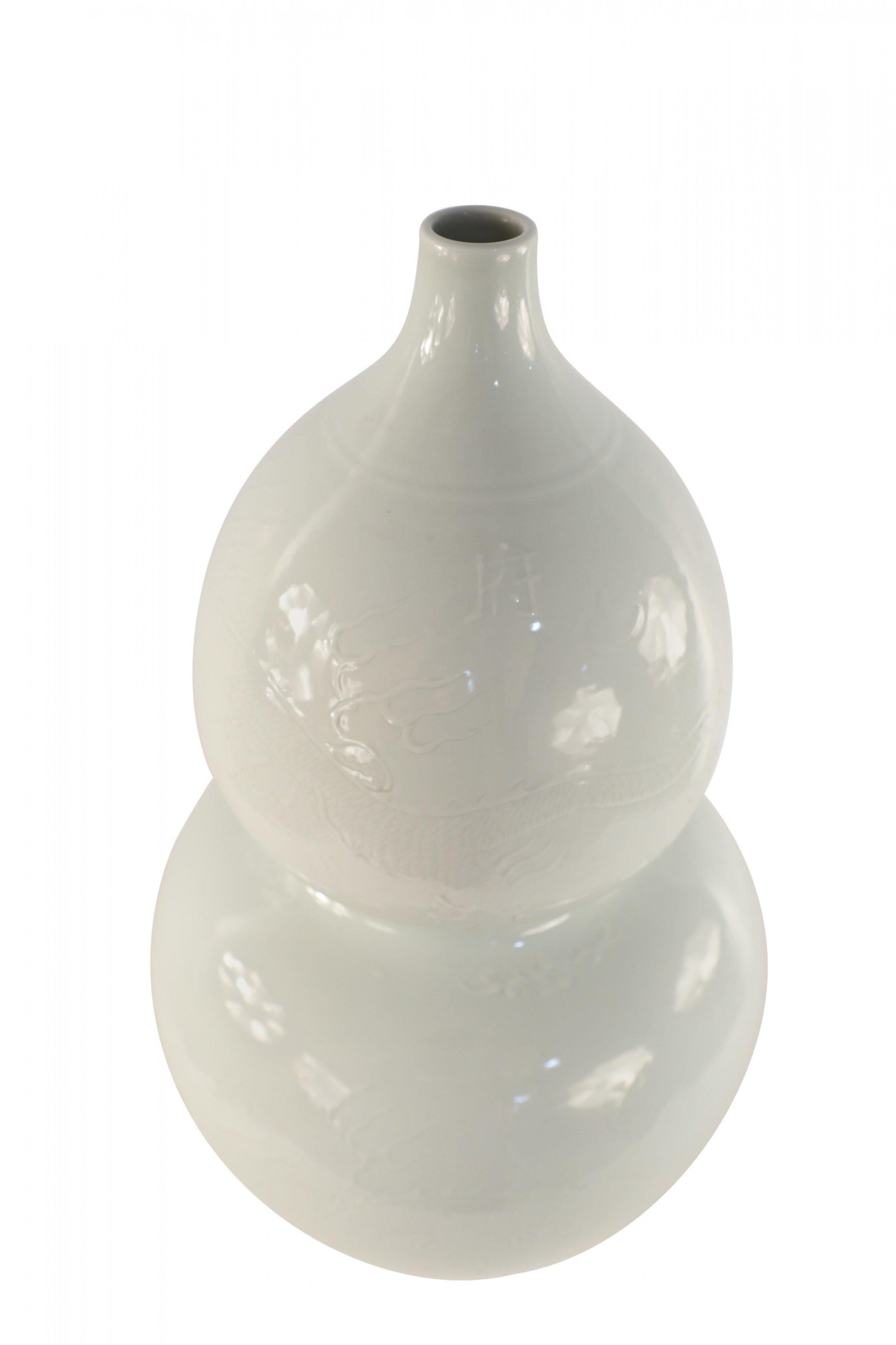 Chinese white, glazed porcelain double gourd bottle thought to bring peace, longevity and happiness to its owner, with a faint etched dragon motif.
 