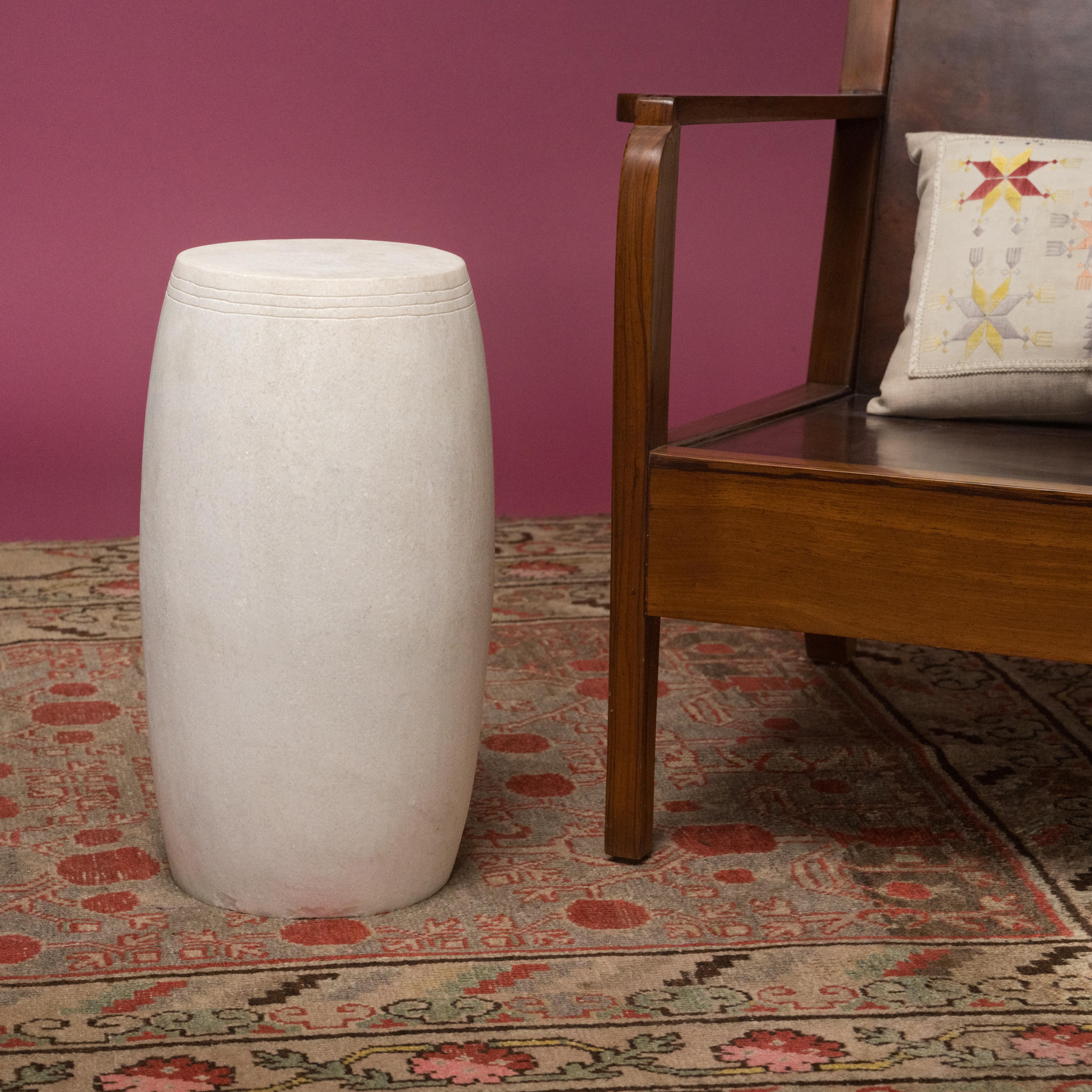This narrow drum stool was carved from a solid block of white marble with a Minimalist tapered design. The stool is subtly etched with thin grooves around the top, suggestive of the lines drawn by stretched hide on an actual drum. Traditionally used