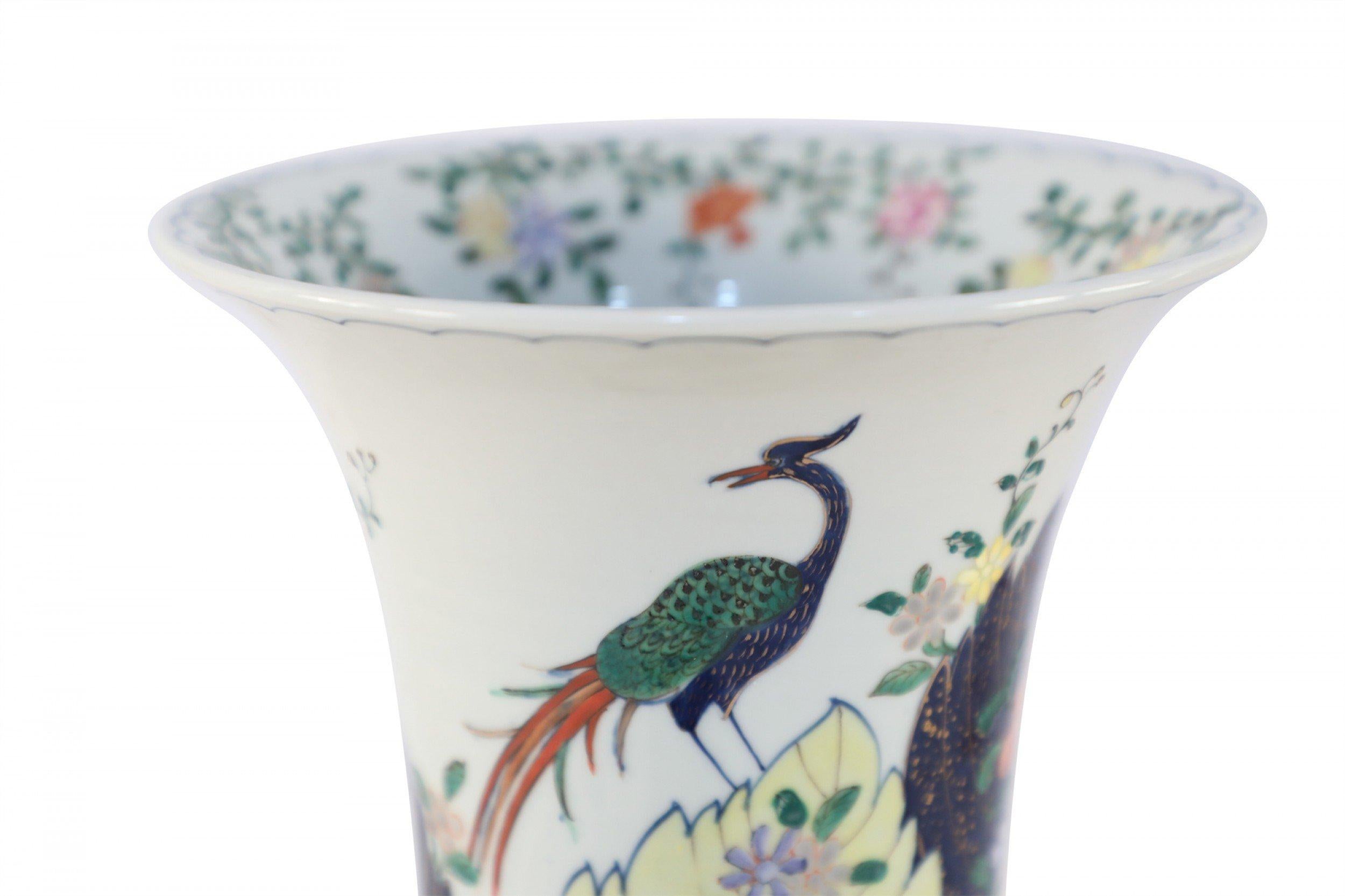 Chinese white porcelain fluted vase with a tall, cylindrical form decorated in large scale dark blue leaves outlined in gold, amid green, yellow and pink foliage and flora topped with a blue peacock, and botanicals painted in the interior.
     