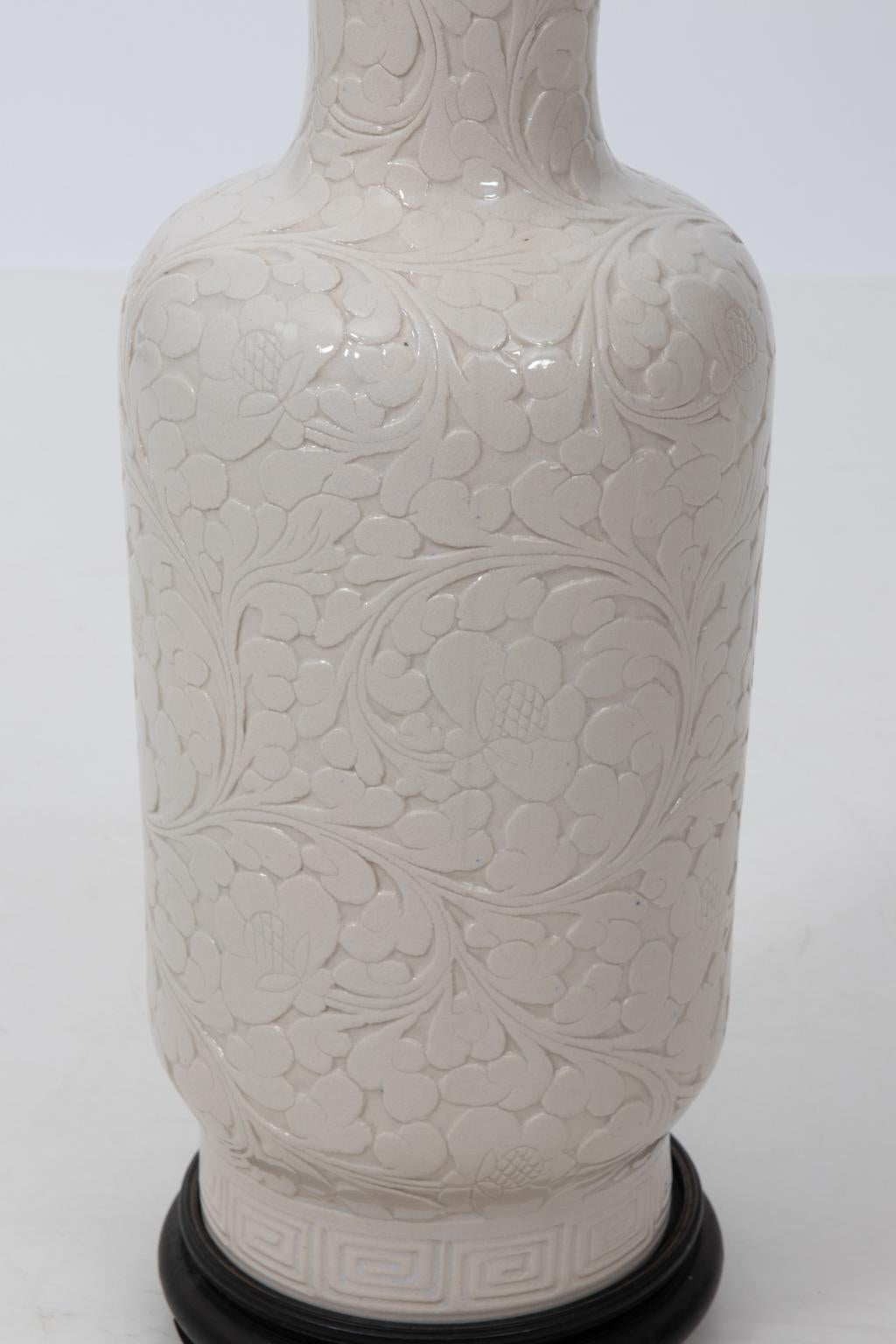 White glazed vase with foliate designs on a black wood base, circa 1970s. Please note of wear consistent with age including finish loss on the body and rim. Made in China.