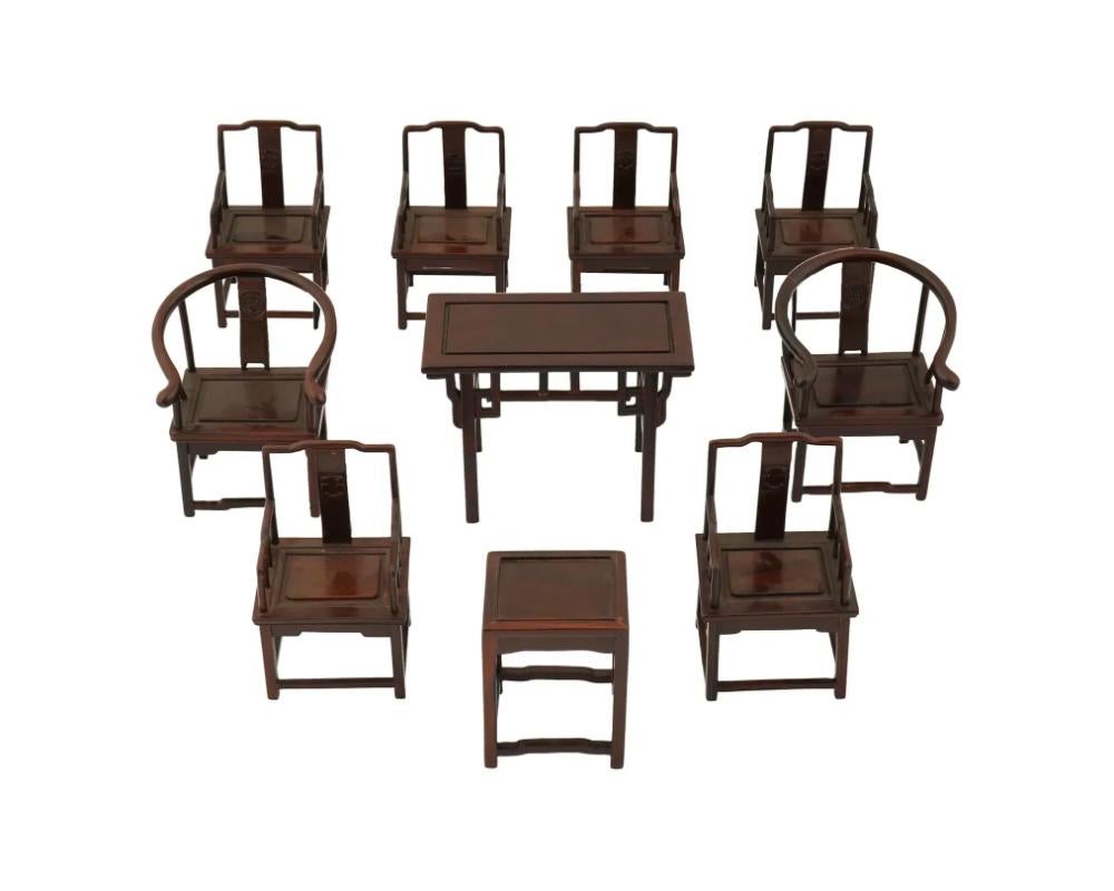 Conjunto de muebles chinos de madera en miniatura diseñados para una casa de muñecas. El conjunto incluye nueve sillas y una mesa, todas ellas de madera oscura con acabado pulido. Las sillas presentan elementos de diseño tradicionales chinos: