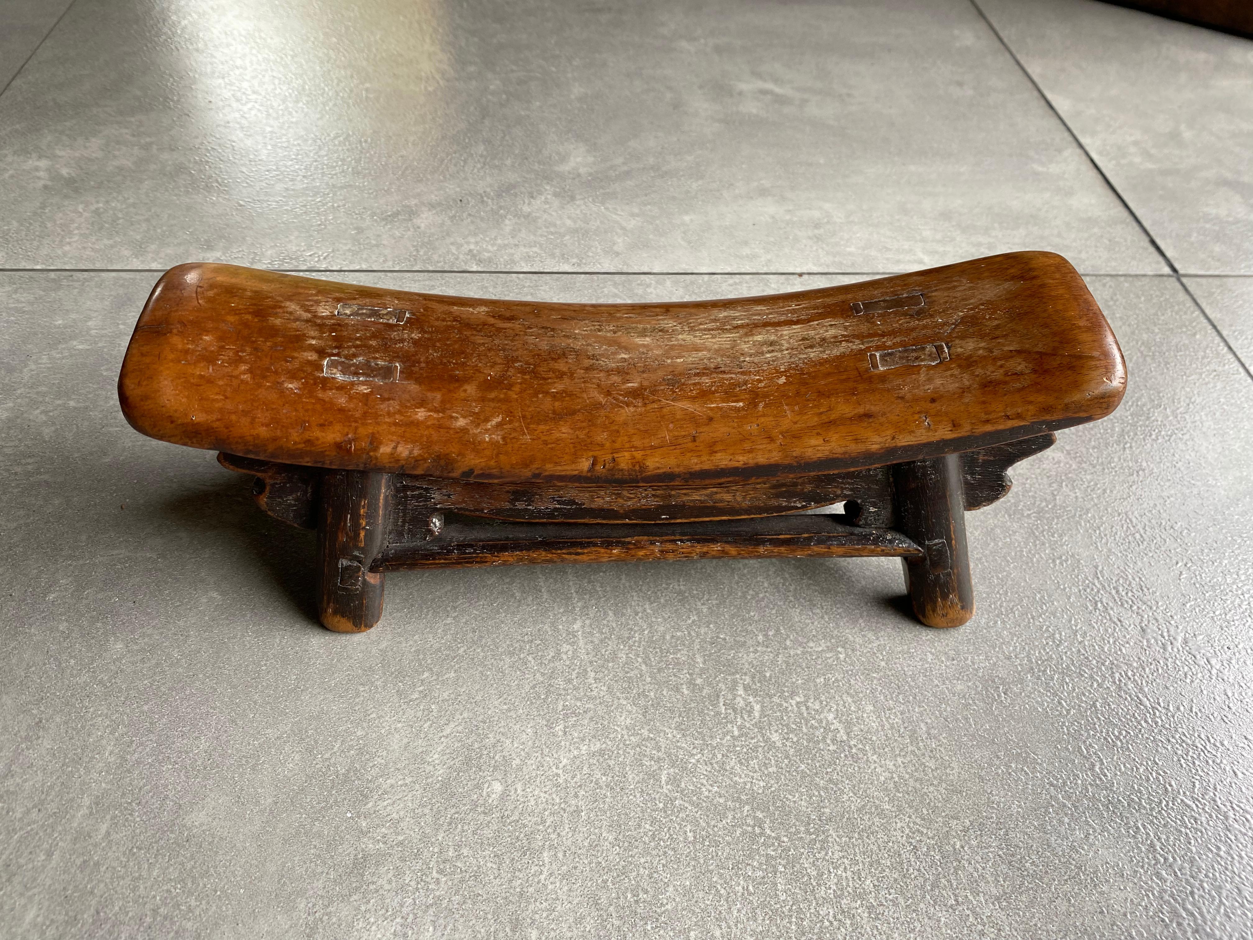 This Chinese headrest was once used in an opium smoke house for a smoker to rest while intoxicated. It is hand-carved from wood with an elegantly curved shape. This piece has a lovely wood texture and was crafted using only wooden