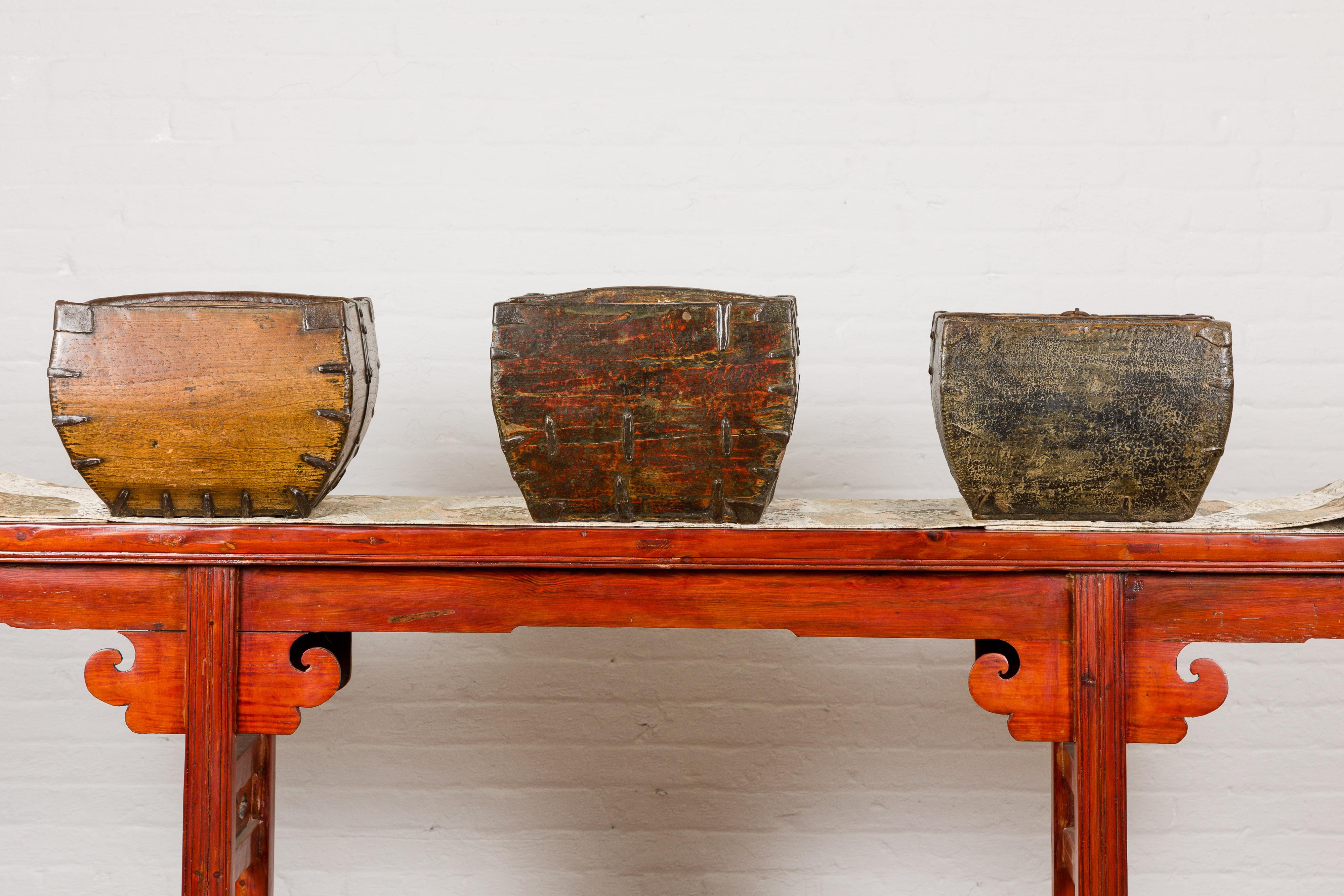 Three rustic Chinese rice measure wooden baskets from the mid 20th century with brown color, handles and metal accents. They are priced and sold individually. Immerse yourself in the rustic charm of these mid-20th century Chinese rice measure