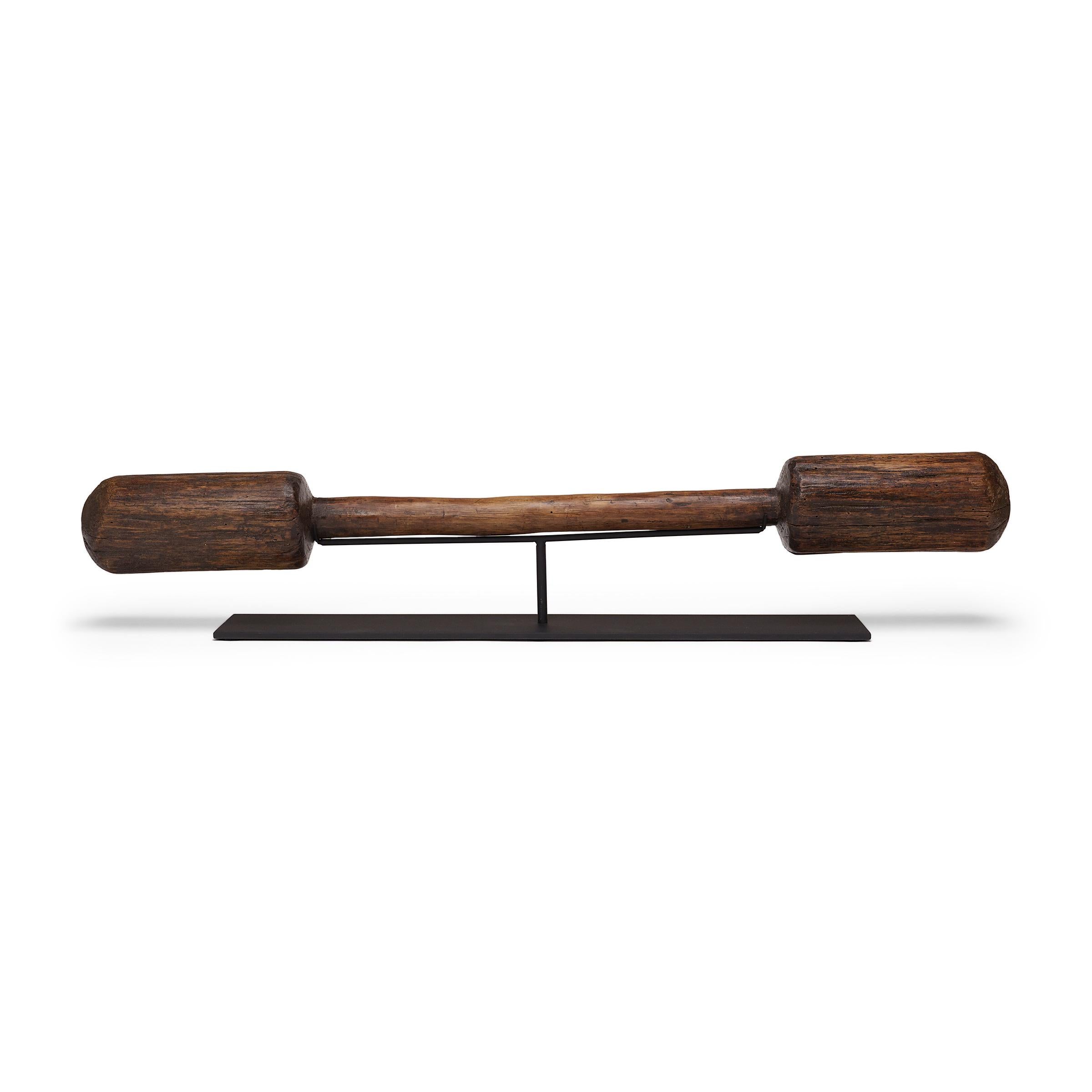 This long wooden object is a 19th century pestle, originally used with a large, free-standing mortar to pound rice or other grains. Placed upon a custom steel mount, the wooden tool lives on as a tabletop sculpture with a unique abstract form and