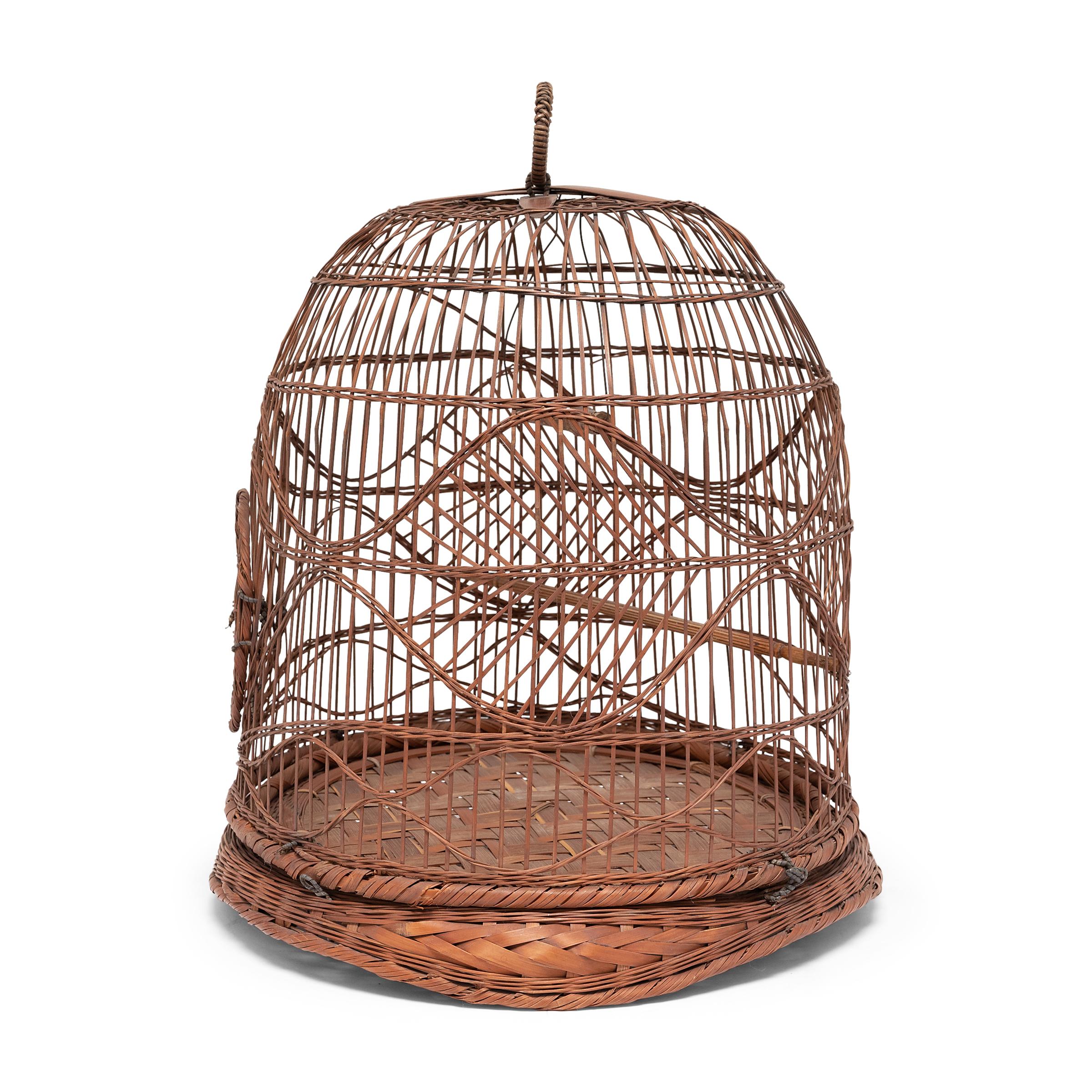 This elegant birdcage is beautifully woven of thin strips of bamboo in the spirit of fine decorative basketry. The horizontal weft wraps around the cage with graceful curves, mirrored by the curved tripod form of the woven base. The cage includes