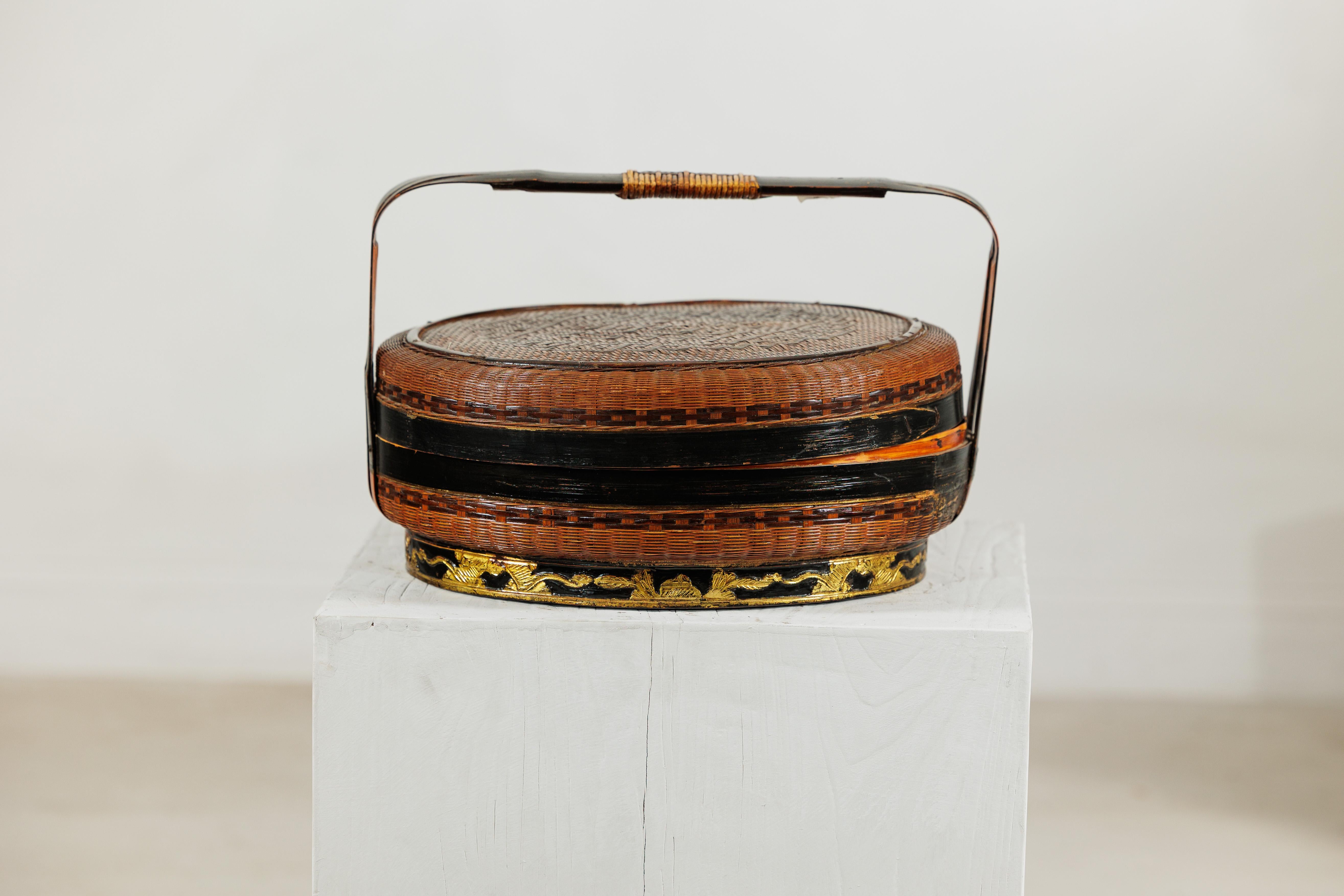 Esta cesta china tejida de finales de la dinastía Qing aúna artesanía y detalles decorativos en una forma que es a la vez funcional y llamativa. El cuerpo redondeado está finamente tejido con fibras naturales, acabado con bandas lacadas en negro que