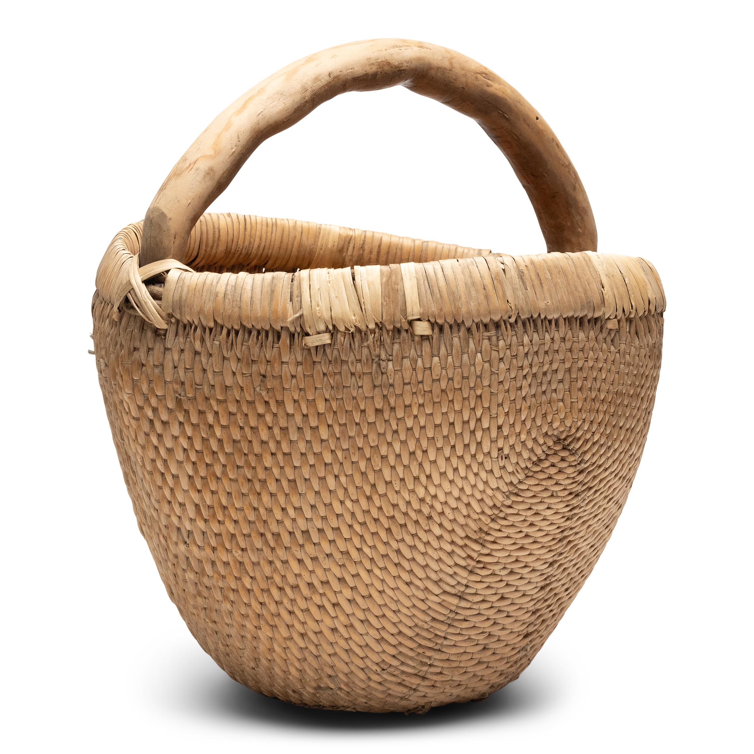 It is easy to imagine someone, long ago, gathering a harvest from their garden or strolling to the market with this beautiful basket tucked under their arm. Hand-woven of young willow branches and twine, the basket has deep, rounded body that tapers