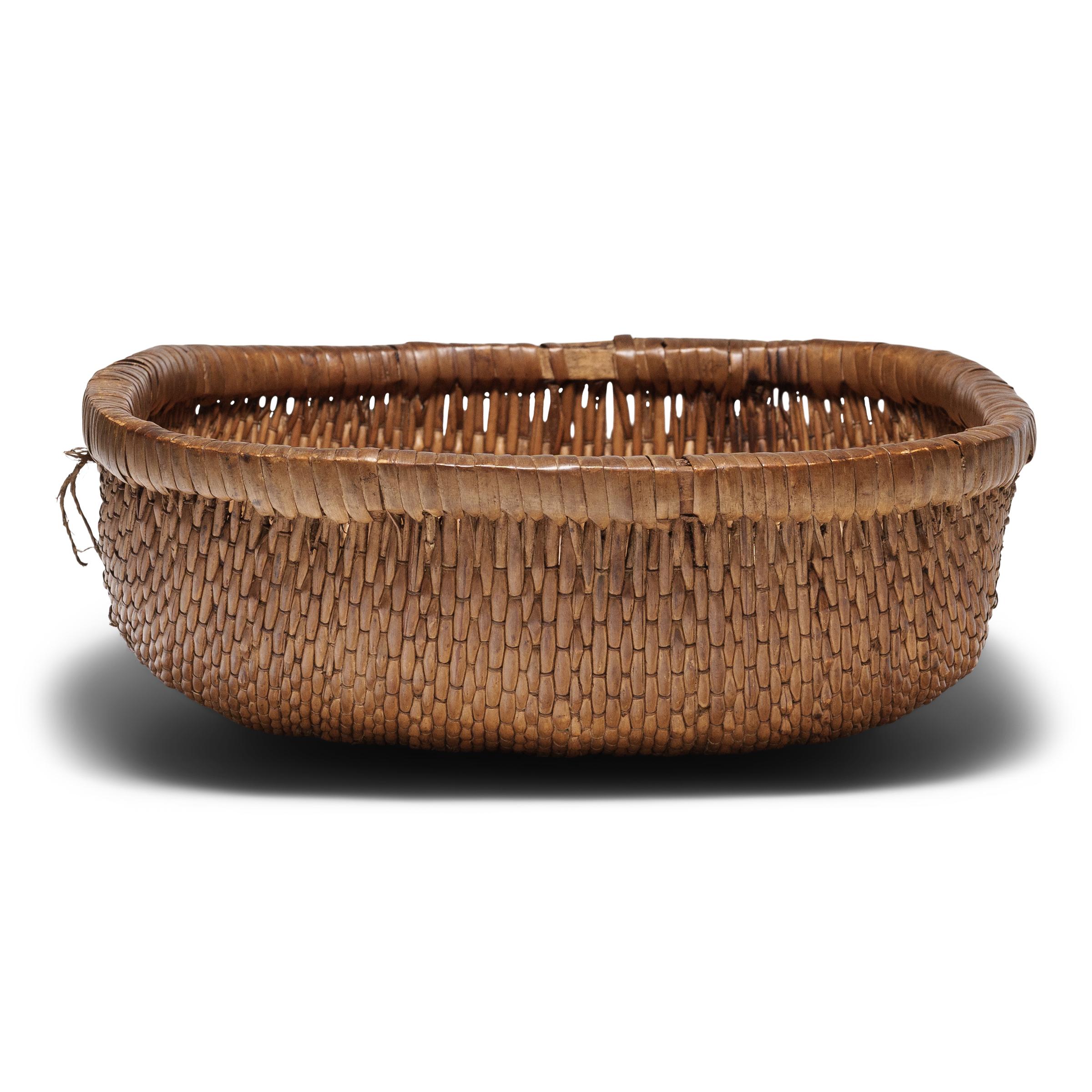 This intricately woven tray basket was originally used for harvesting grains or in a kitchen for food prep and storage. Despite its humble origin, the basket exhibits remarkable workmanship, beautifully woven by hand of willow and cord around a bent