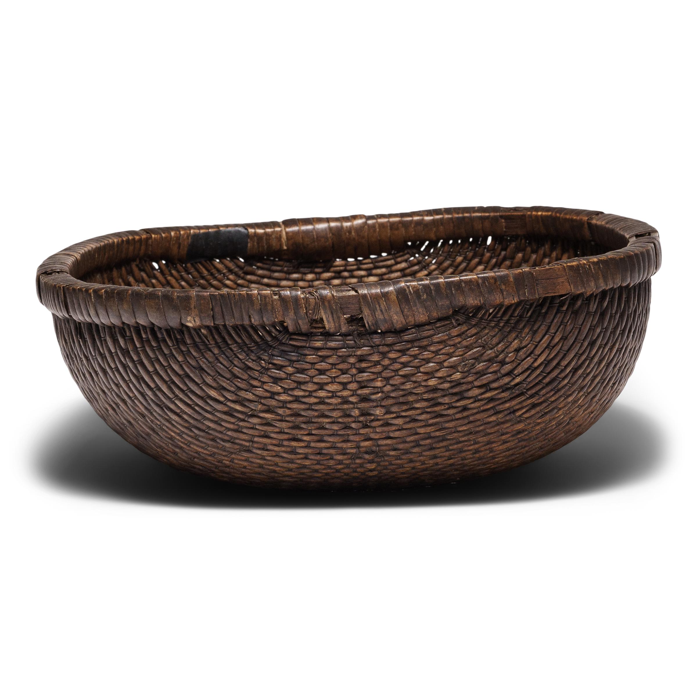 This intricately woven tray basket was originally used for harvesting grains or in a kitchen for food prep and storage. Despite its humble origin, the basket exhibits remarkable workmanship, beautifully woven by hand of willow and cord around a bent