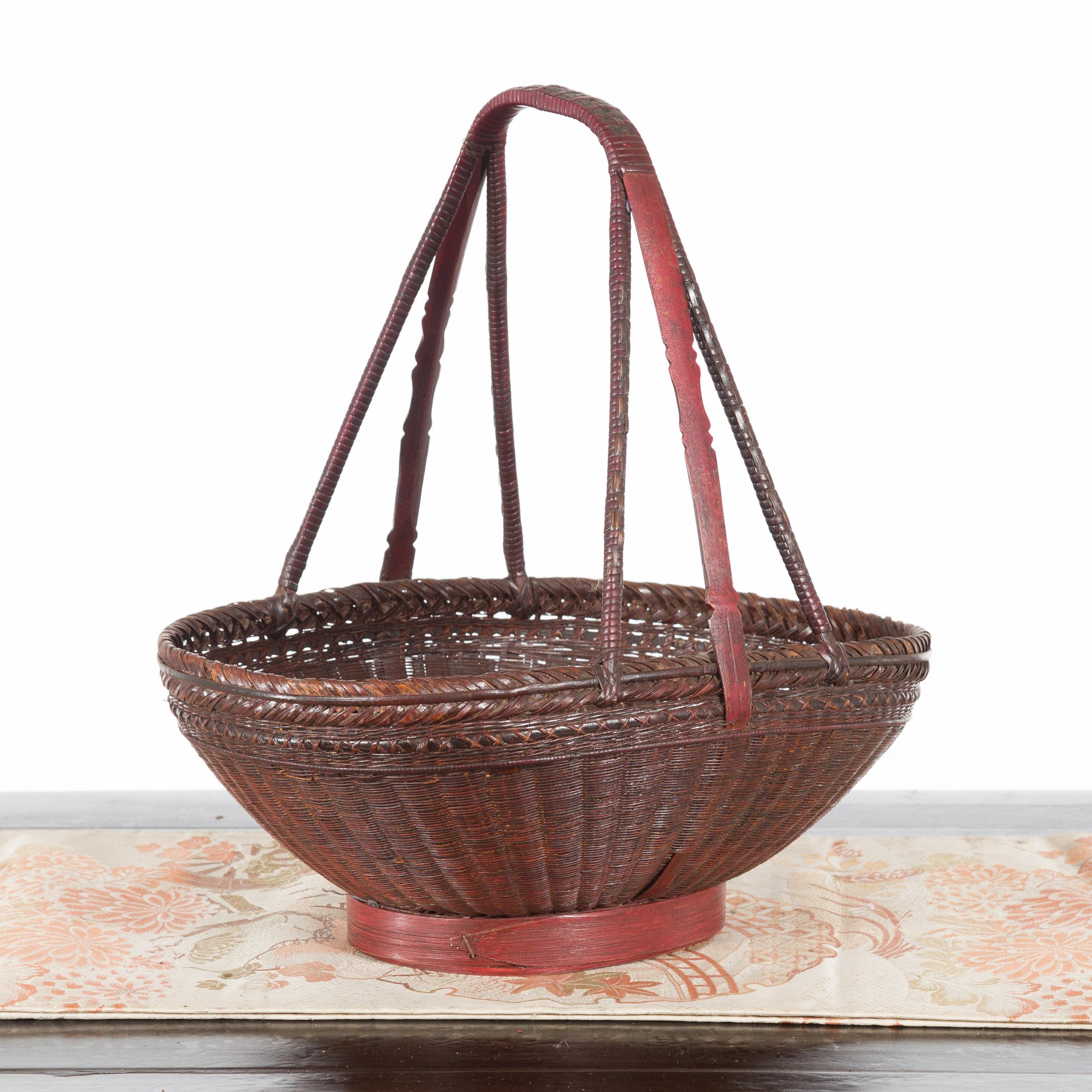 An early 20th century rattan woven market basket with a carrying handle from China. With red and dark brown colors throughout the antique basket, the handwoven rattan stitching makes for a beautiful display of craftsmanship and precision. The tall