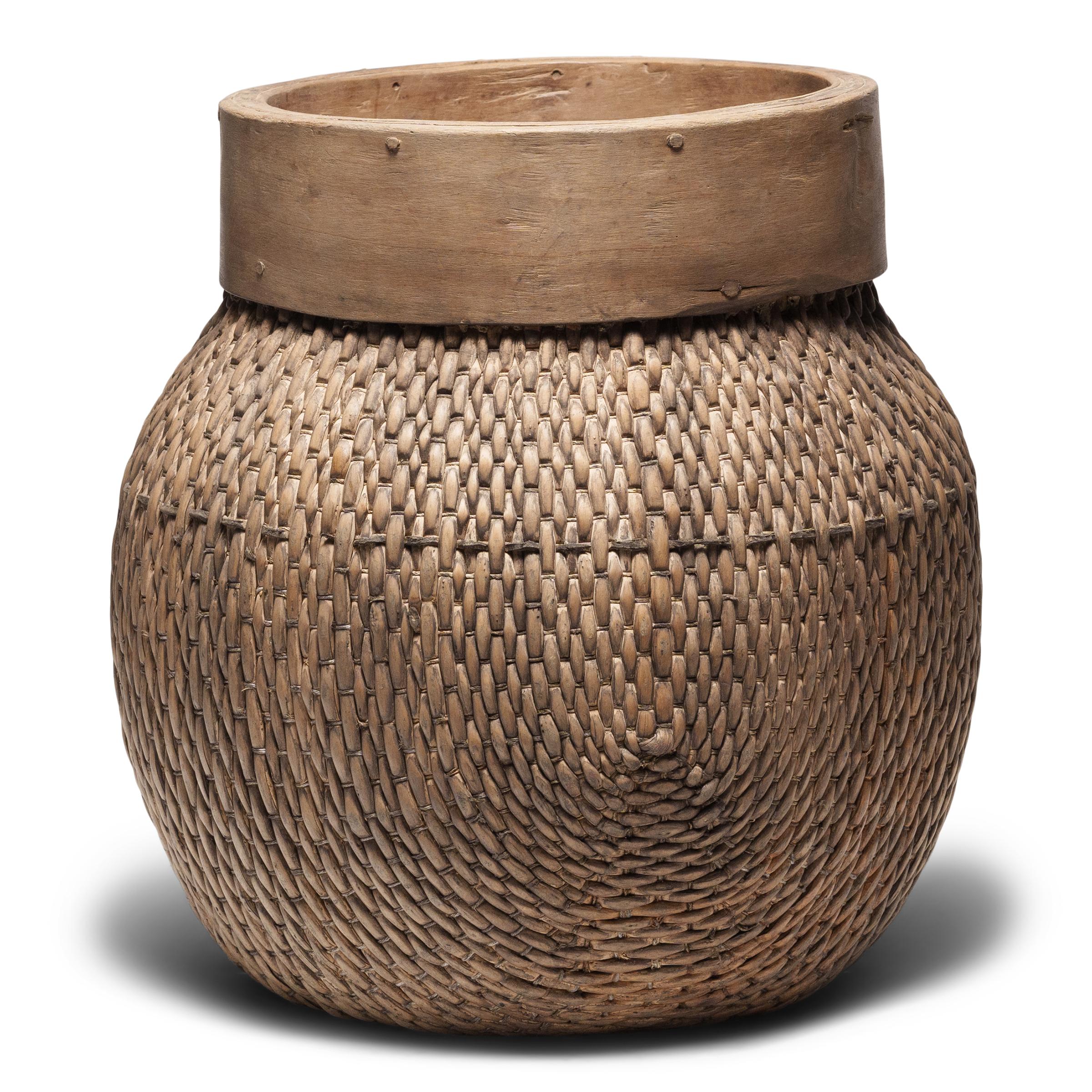 Centuries ago, a woven reed fisherman’s basket such as this would have been common in rural China as an everyday item, used until it became worn through. This hand-woven example has a squat, rounded form and features a woven body secured to a